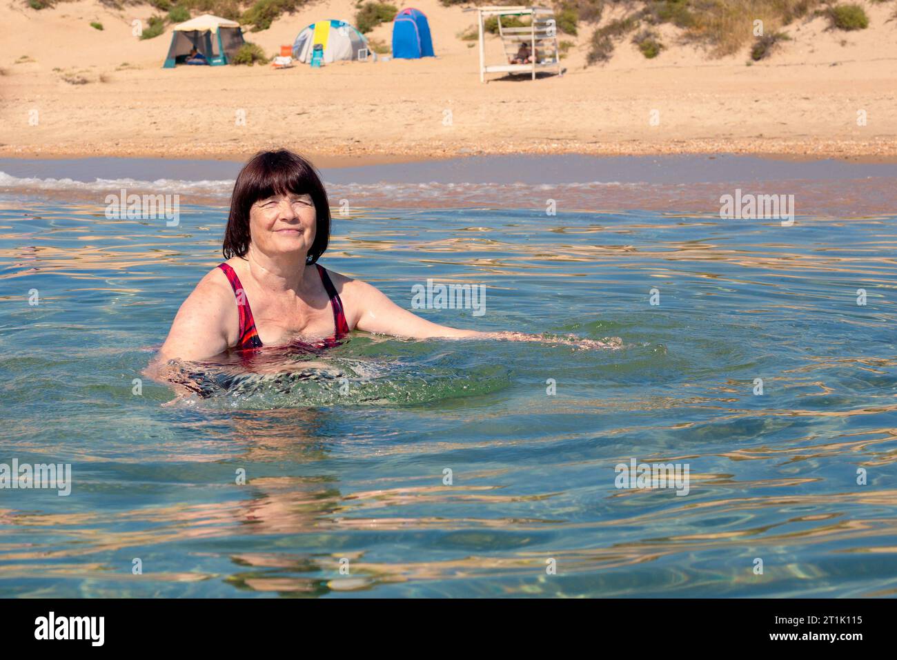 An older woman swims in clear sea water. Sea holiday on the shore. Stock Photo