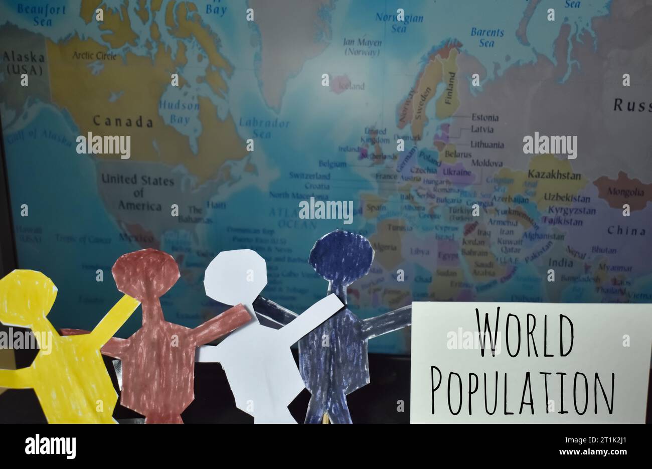 A close up picture of various races people paper dolls in front of a word map. World population day concept Stock Photo