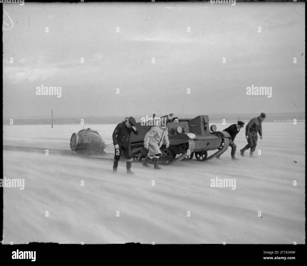 The Royal Navy during the Second World War The naval mine recovery and disposal squad underway with the mine under tow by a Polish Bren gun carrier at Tayport. A strong wind is whipping up the sand whilst the squad walk with their heads bowed into the wind. Stock Photo