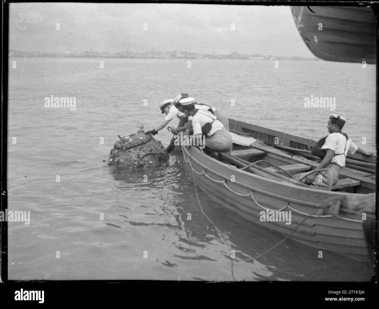 The Royal Navy during the Second World War Sailors in a small rowing boat shackle a floating mine to a towing wire so it can be rendered safe at Singapore. Stock Photo