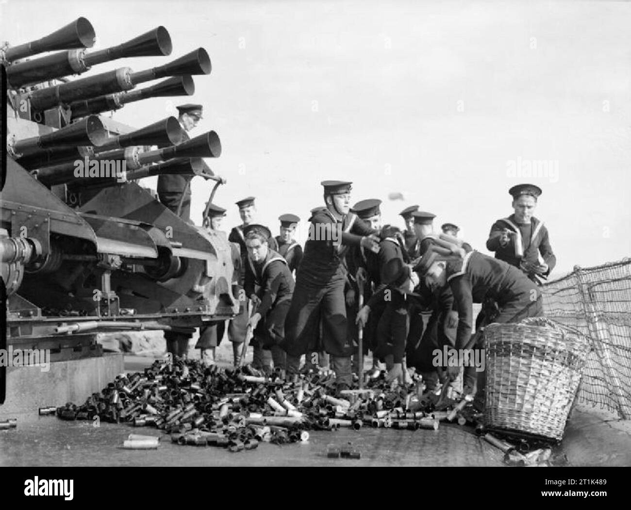 The Royal Navy during the Second World War Naval ratings, under the watchful gaze of a NCO (left) sweep up spent cartridge cases for the eight barrelled, Vickers two pounder Mark VIII 'pom pom' gun. These ratings were firing live ammunition at the anti-aircraft gunnery school, Portsmouth Harbour. Stock Photo