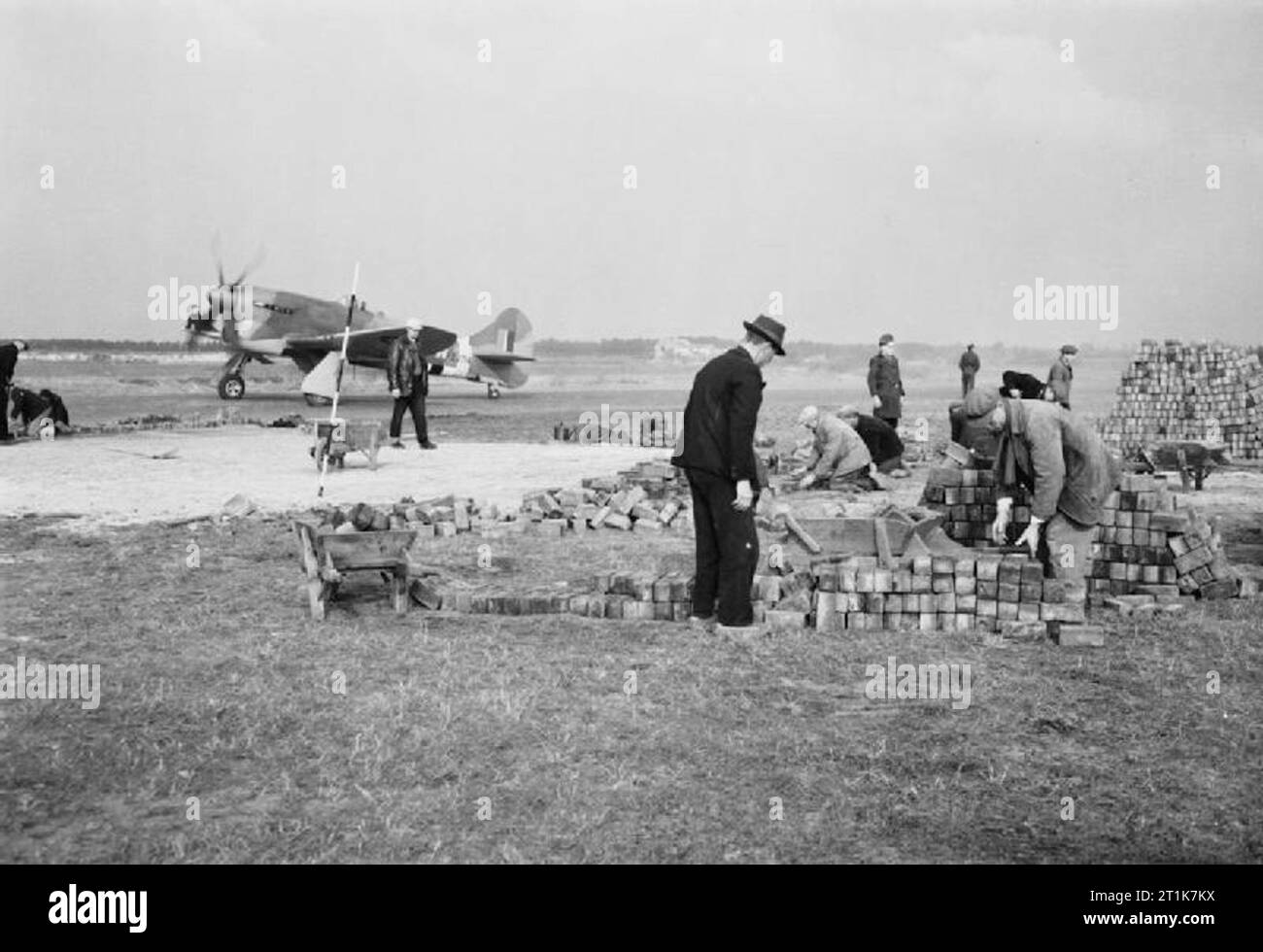 Royal Air Force 1939-1945- Fighter Command Dutch labourers use bricks to create a dispersal point at Volkel (B-80), 24 October 1944. In the background a No 274 Squadron Tempest (EJ714/JJ-W) taxies out for another defensive air patrol over the battlefront. Volkel was home to No 122 Wing until April 1945, when the Tempest squadrons relocated to bases on German soil. Stock Photo