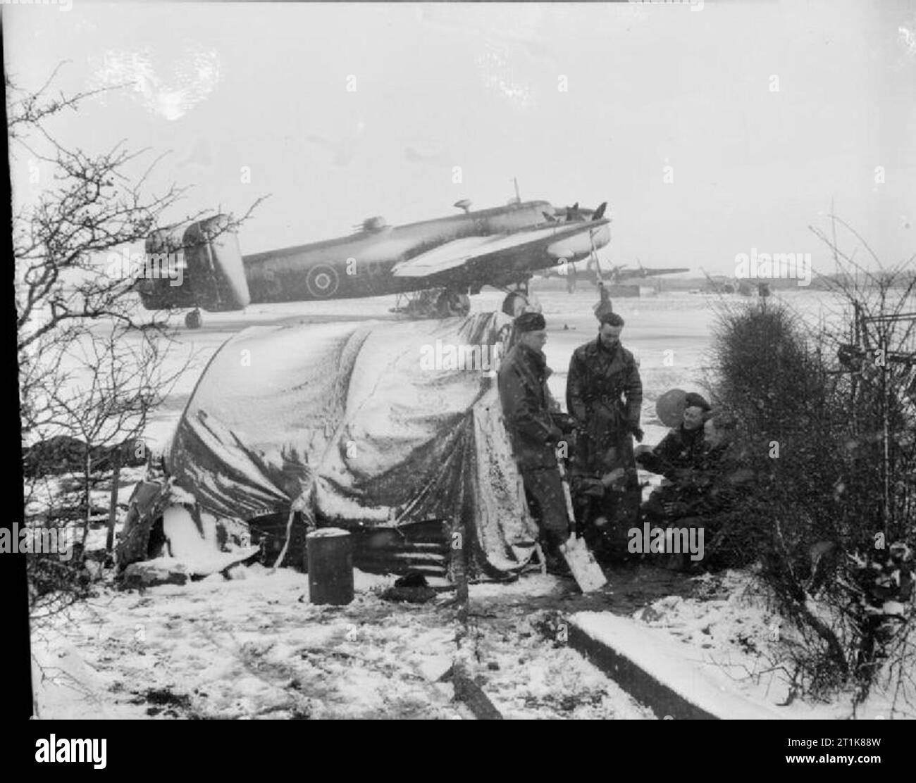 Royal Air Force Bomber Command, 1942-1945. Ground crew warm themselves on a stove in the snow at Rufforth, Yorkshire, before venturing onto the dispersal behind them to service a Handley Page Halifax of No. 1663 Heavy Conversion Unit. Stock Photo