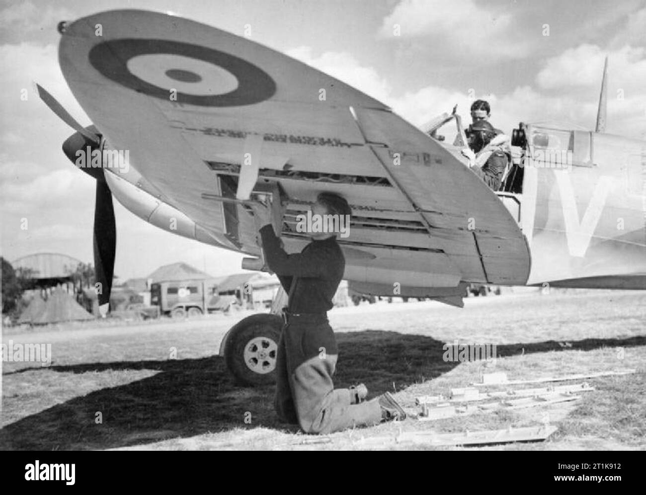 Royal Air Force Fighter Command, 1939-1945. Armourer Fred Roberts re-arms Supermarine Spitfire Mark IA, X4474 'QV-I', of No. 19 Squadron RAF at Fowlmere, Cambridgeshire, while the pilot, Sergeant B J Jennings, has a word with his mechanic. Manor Farm can be seen in the background. Stock Photo