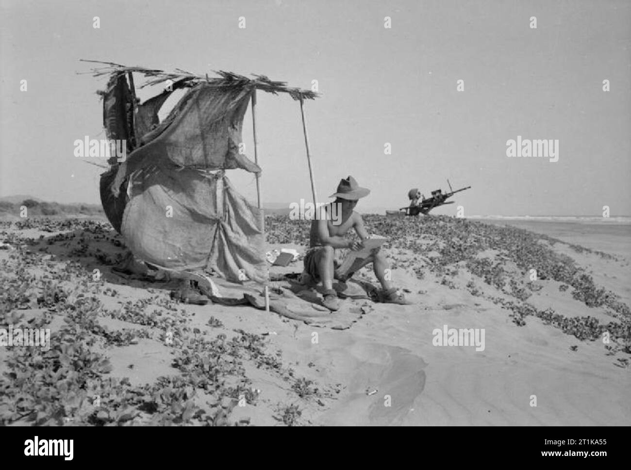 Royal Air Force Operations in the Far East, 1941-1945. An RAF Regiment anti-aircraft gun team on duty by the beach airstrip at Nidania ('George') on the coast of Bengal, India: Corporal R Pollard of Whimple, Devon, stands down to receive a letter from home as Leading Aircraftman Reeve of Newcastle-on-Tyne mans the 20mm Hispano light anti-aircraft gun Stock Photo