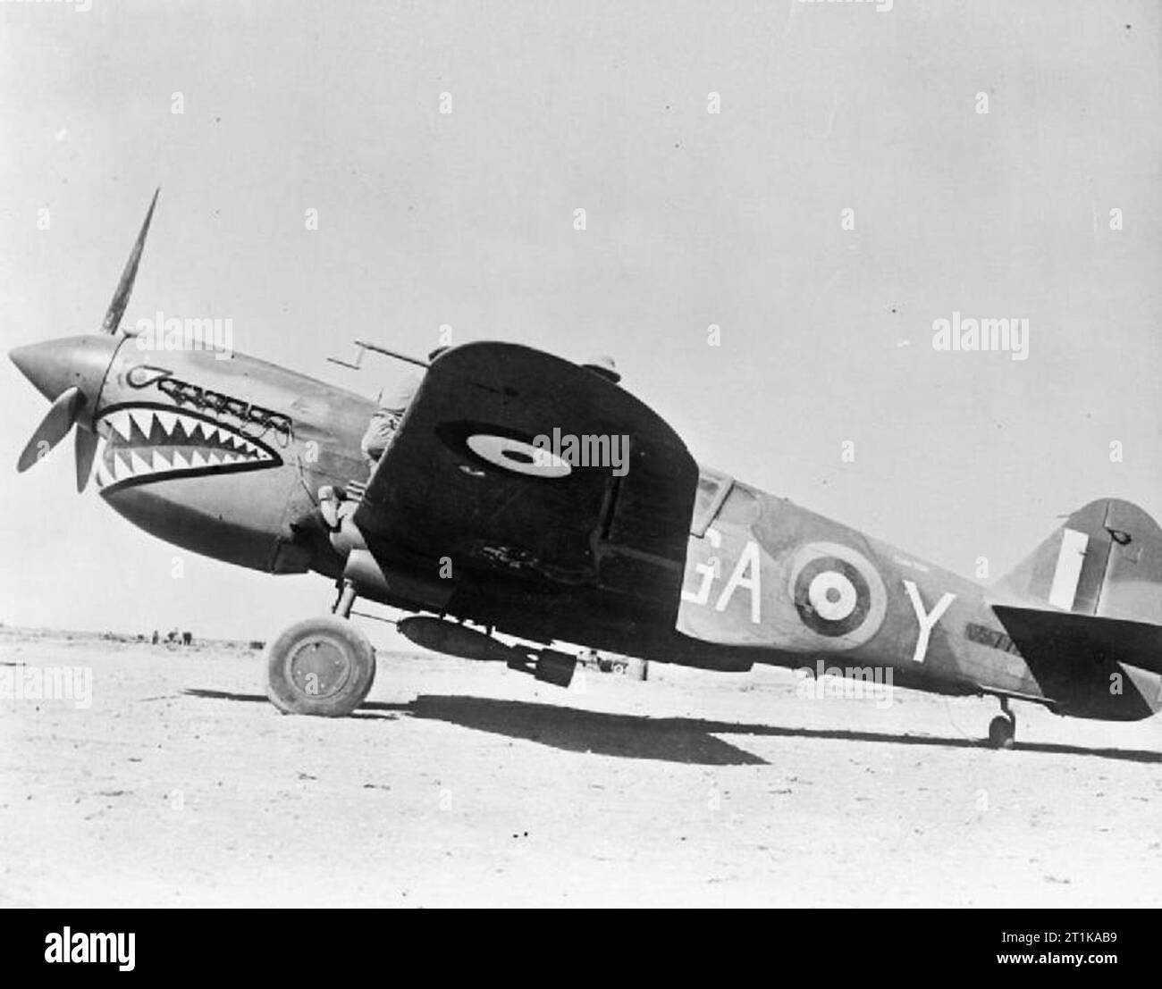 Royal Air Force Operations in the Middle East and North Africa, 1939-1943 Curtiss Kittyhawk Mark I, AK772 'GA-Y' 'London Pride', of No. 112 Squadron RAF is prepared for a sortie at Gambut Main, Libya. The ground crew can just be seen assisting the pilot to strap himself into the cockpit. The aircraft is carrying a 250-lb GP Bomb, fitted with a surface-burst impact fuse, under the fuselage. Note also the plugs placed in the exhaust stubs to keep the desert sand out. AK772 was lost on a ground attack mission near Bir Hacheim on 30 May 1942; its Australian pilot, Pilot Officer H G Burney, was kil Stock Photo