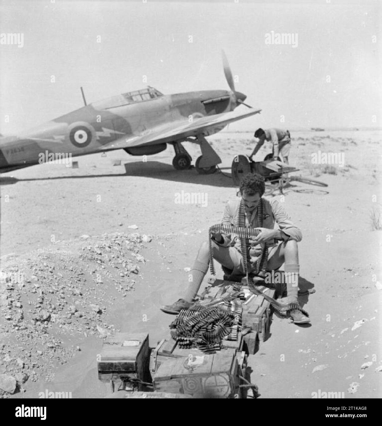 Royal Air Force Operations in the Middle East and North Africa, 1939-1943. Sergeant Pilot F H Dean of No. 274 Squadron RAF examines belts of .303 ammunition before they are installed in his aircraft at Sidi Barrani, Egypt. In the background, one of the groundcrew attaches a trolley-accumulator to Hawker Hurricane Mark I, P2638, sporting the yellow lightning flash emblem (later changed to blue) which became 274 Squadron's unofficial insignia at about this time. Sergeant Dean was shot down and killed on 15 May 1941, when his section of Hurricanes fought with Messerschmitt Bf 109s near Halfaya at Stock Photo