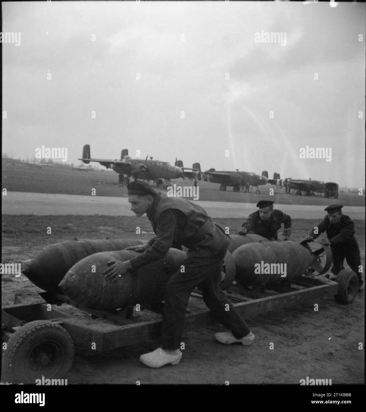 Royal Air Force- 2nd Tactical Air Force, 1943-1945. Ground crew of the Royal Dutch Naval Air Service, serving with No. 320 (Dutch) Squadron RAF, push a trolley of 1,000-lb MC bombs to waiting North American Mitchells at B58/Melsbroek, Belgium. Leading Aircraftman Jan Sieben, in the foreground, is wearing 'klompen' (clogs). Stock Photo