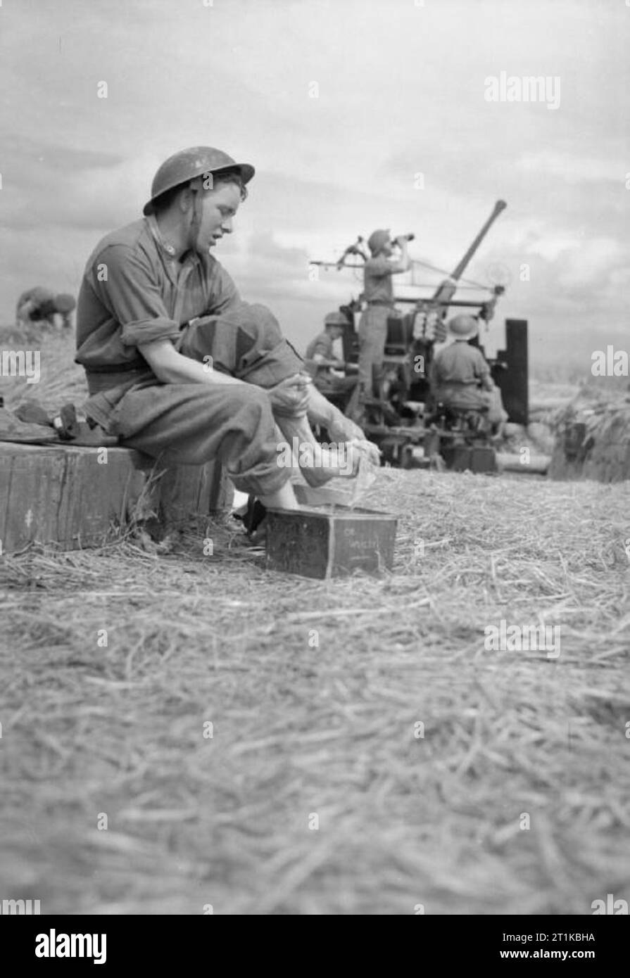 Royal Air Force- 2nd Tactical Air Force, 1943-1945. Leading Aircraftman Ernie Hulstone of the RAF Regiment washes his feet in a biscuit tin while other members of his squadron man a 40mm Bofors anti-aircraft gun at B5/Le Fresne Camilly, Normandy. Stock Photo