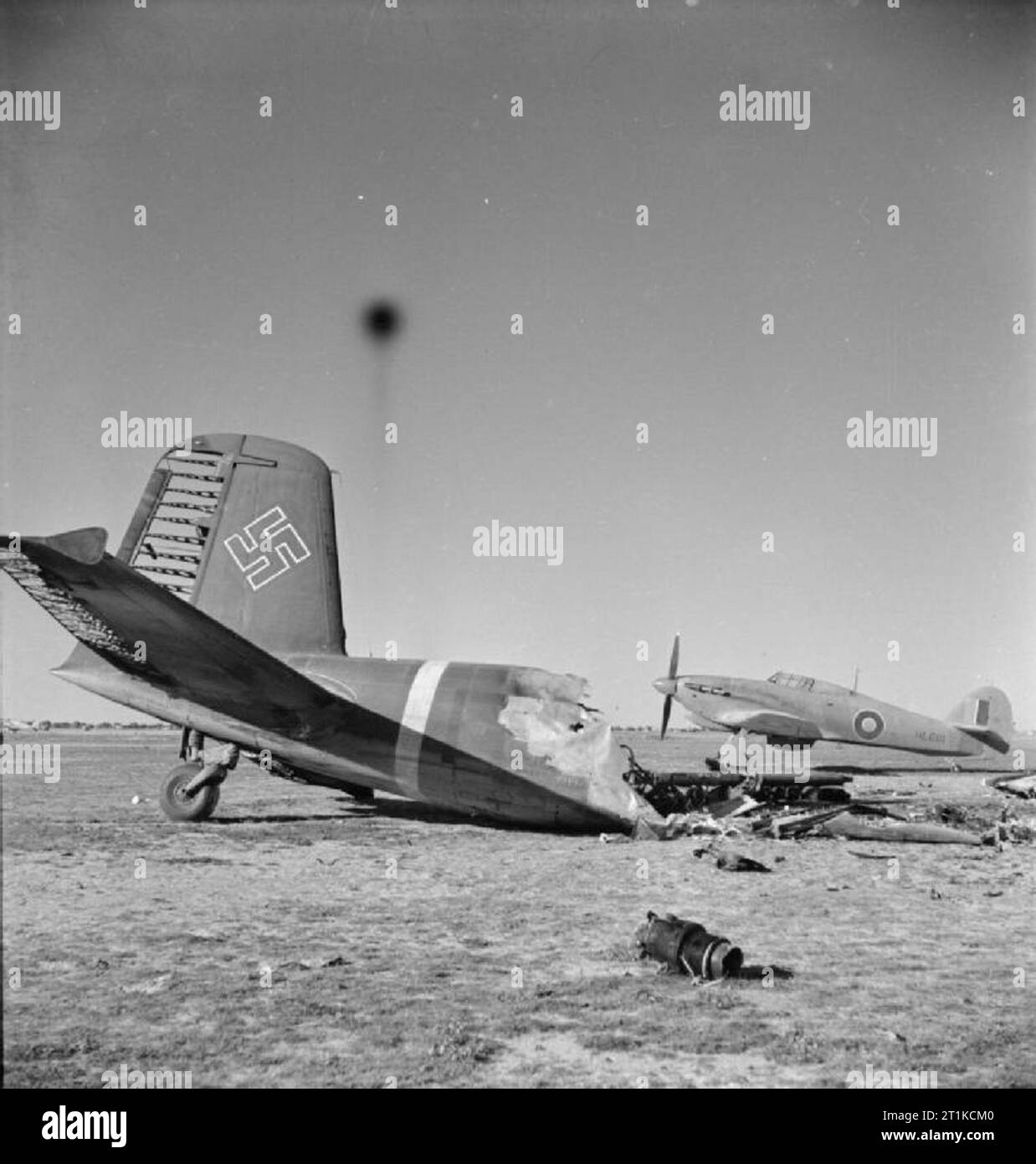 Royal Air Force- Operations in the Middle East and North Africa, 1939-1943. Behind the wreckage of a burnt-out Focke Wulf FW 200 Condor, Hawker Hurricane Mark IIB, HL681 'A', of No. 274 Squadron RAF, stands on the landing ground at Castel Benito, Tripolitania, after its capture. 274 Squadron were temporarily installed there until the airfield at Mellaha could be made serviceable for use. Stock Photo