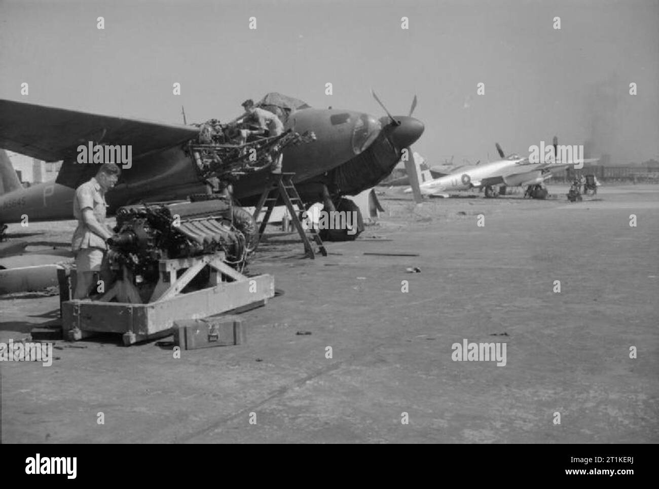 Royal Air Force Operations in the Far East, 1941-1945. Fitters of No. 684 Squadron RAF prepare to install a new Rolls Royce Merlin 76-series engine in De Havilland Mosquito PR Mark XVI, NS645 'P', at Alipore, India. NS645 is finished in overall 'PR blue' paint scheme, while in the background another aircraft of the Squadron, MM367 'M', has a silver dope finish with local theatre recognition markings. Stock Photo