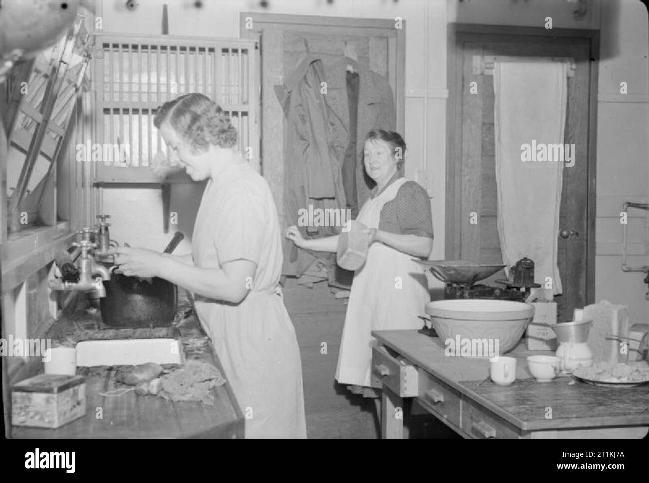 Chipstead Council School- Education and Communal Feeding, Chipstead, Surrey, 1942 Head cook Mrs Oxenham (right) and assistant cook Mrs Hallowes at work in the kitchen at Chipstead Council School. Mrs Hallowes, who has a husband in the Army and a child at the school, appears to be washing vegetables. Mrs Oxenham holds a loaf of bread. Stock Photo