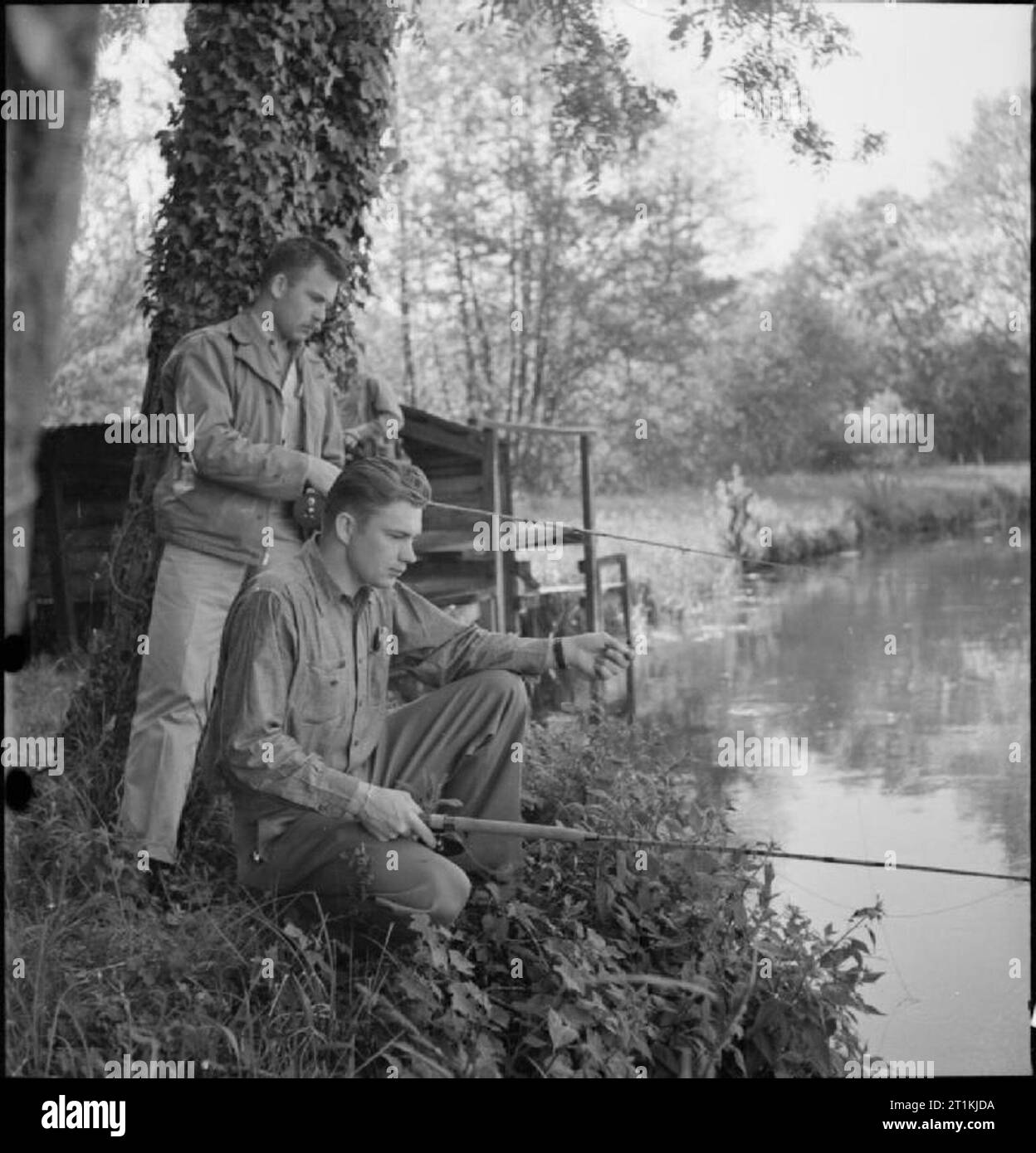 Country Club For US Airmen- Rest and Recuperation in the English Countryside, Stanbridge Earls, Romsey, Hampshire, 1943 Lieutenant J D Baird (standing) and Captain J R Bullock enjoy a spot of trout fishing on the banks of the River Test in Hampshire. Lieutenant Baird is the pilot of a 'Fort' (B17 Flying Fortress) from Suring, Wisconsin and Captain Bullock is a B17 navigator from Greensboro, North Carolina. According to the original caption: 'These fighters expected trout fishing to bore them, were genuinely surprised and pleased by the enjoyment it gave in spite of little success in the shape Stock Photo