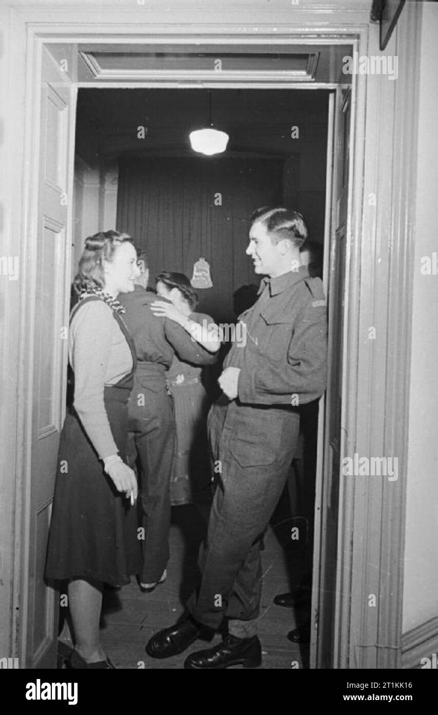 Entertainment in Wartime Britain, 1941 A young woman chats to a soldier as they stand in the doorway of a room. They are attending a dance party which is being held in a house or hostel, somewhere in Britain. Stock Photo