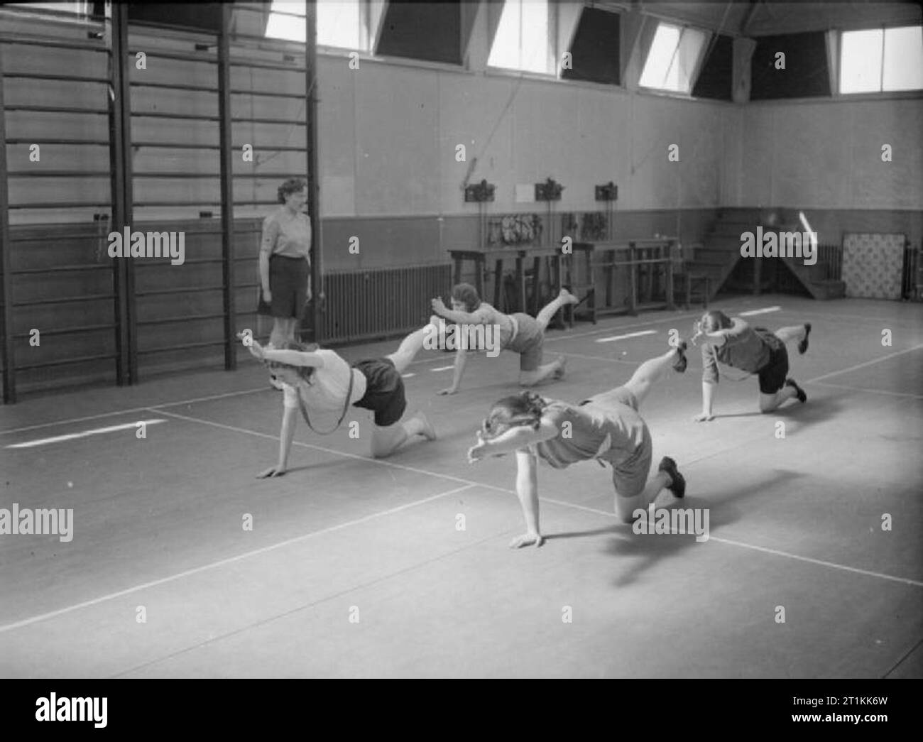 Factory Welfare Work- Welfare at Pilkington's Glass Factory, St Helens, Lancashire, England, UK, 1944 Women do stretching exercises in the gymnasium at the factory rehabilitation centre, (probably at Pilkington's glass works at St Helens), as part of their recovery after an injury. They are kneeling on the floor, with one leg and the opposite arm outstretched. According to the original caption 'the aim of [the centre] is to prevent men and women from becoming permanently disabled. By exercises and massage under the guidance of a physio-therapist trained in modern methods the injured persons ar Stock Photo