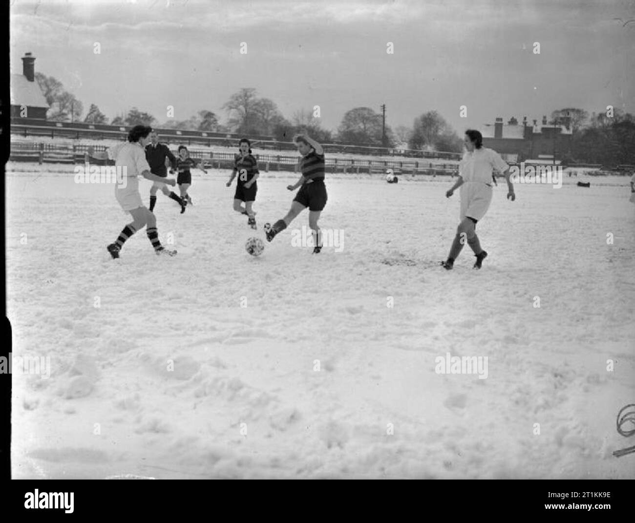 Faireys Play Soccer- a Women's Football Match Between Fairey and Av Roe, Fallowfield, Manchester, Lancashire, England, UK, 1944 A player of the Fairey team (striped jersey) kicks the ball as two members of the AV Roe team (white jerseys) run in from either side. The match is taking place on the snow-covered pitch of Manchester Athletic Club's ground at Fallowfield. Stock Photo
