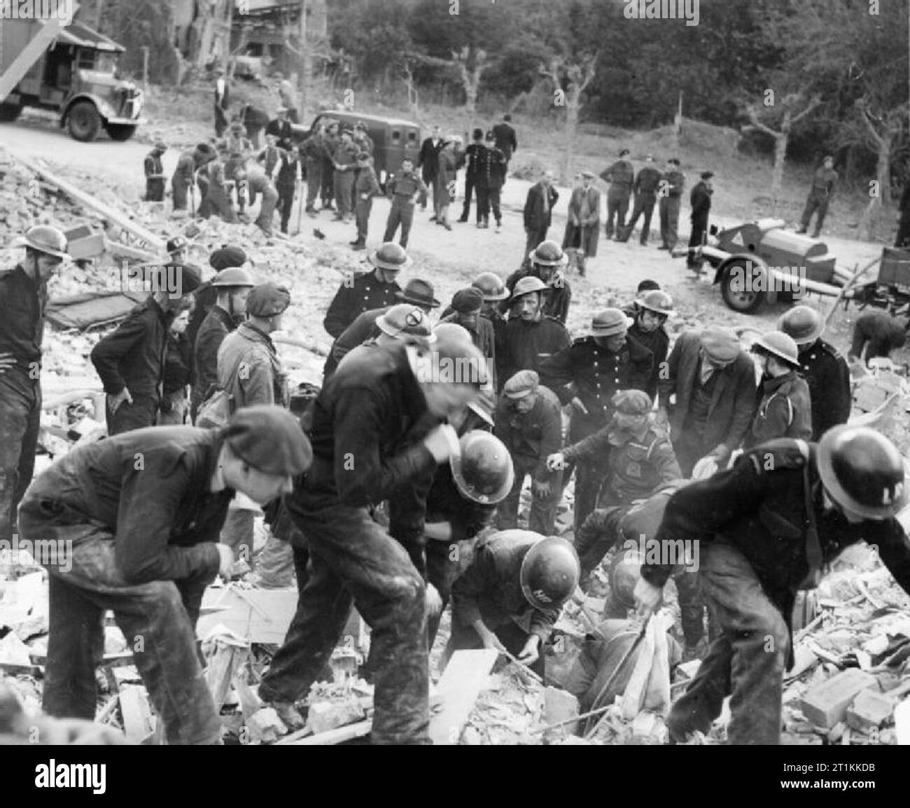 Flying Bomb- V1 Bomb Damage in London, England, UK, 1944 Civil Defence rescue workers search for survivors under a huge pile of rubble and timbers following a V1 attack in the Highland Road and Lunham Road area of Upper Norwood. In the background, an ambulance of the American Ambulance Great Britain, several police officers and a National Fire Service trailer pump can be seen. In addition, a group of men of the Pioneer Corps are also visible in the top left hand corner. They are waiting for instructions on where to dig from the rescue squads. Stock Photo