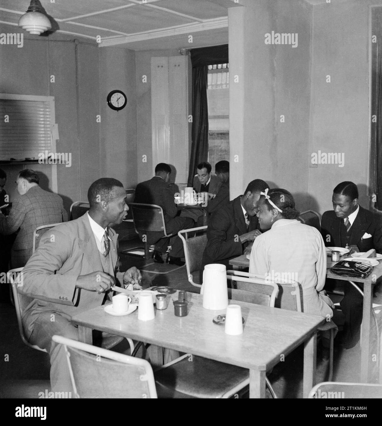 In the basement restaurant of the Colonial Centre at 17 Russell Square, London, civilians from Sierra Leone enjoy a meal, 1944. In the basement restaurant of the Colonial Centre at 17 Russell Square, men and women enjoy a meal. Mr P Thorpee (left) leans across to speak to Miss Rosamund Harding, sitting at a table with Mr D A Thomas and Mr C O E Cole. All four are from Sierra Leone: Mr Thorpee is the chief fire-officer back home, Miss Harding is a student teacher, and Mr Thomas and Mr Cole are law students. The original caption states that the restaurant is painted bright yellow! Stock Photo