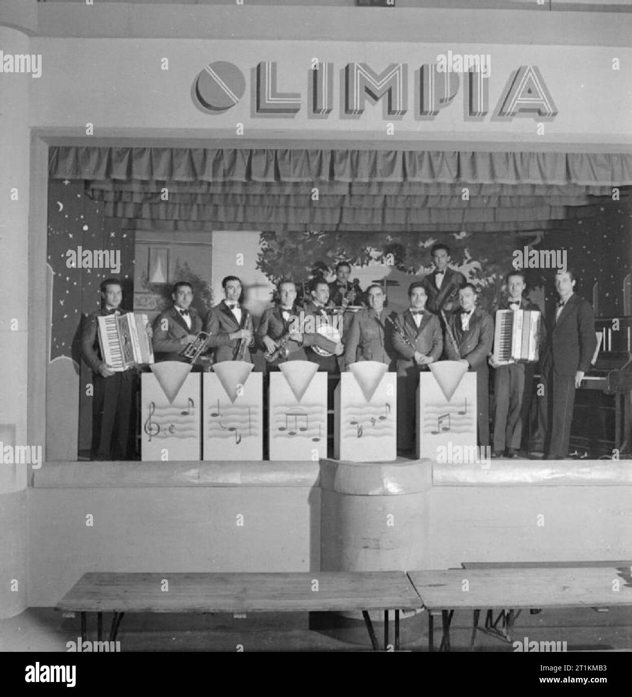 Italian Prisoners of War in Britain- Everyday Life at An Italian Pow Camp, England, UK, 1945 At the N.144 Italian workers camp, near London, the famous 'Seven Dwarves' orchestra pose with their instruments on the stage under a sign reading 'Olimpia'. Amongst the musicians are: Fernando Monticelli, Maestro Aldo Morbido, Salvatore Corsaro, Matteo Giannattasio, Carlo Forno, Alveste Migliorini, Amelio Salvadori, Vincenzo Verrecchia, Salvatore Mastria and Umberto Latini. The dance band includes a saxophone, two accordions, banjo, and piano. Stock Photo