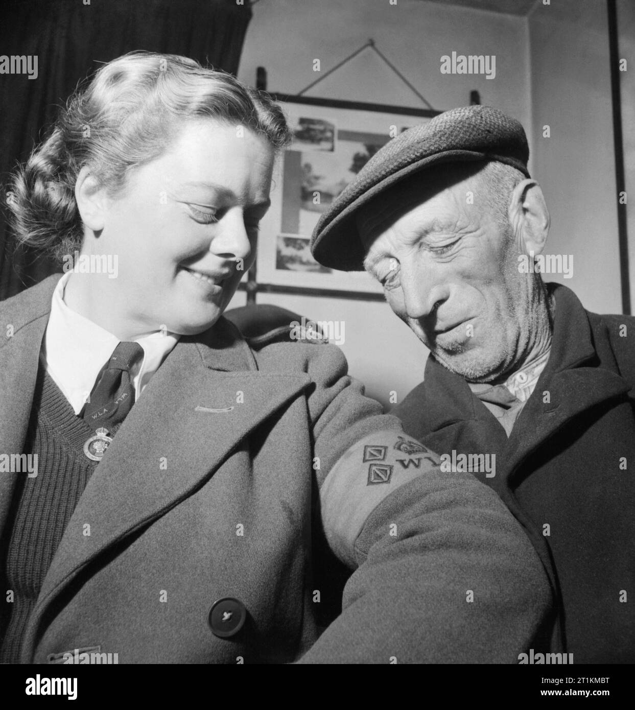 Land Girl Rosalind Cox shows her Women's Land Army armband to local farm labourer Sam Scott in the &quot;Black Dog and Duck&quot; pub at Bury in West Sussex, 1944. Stock Photo