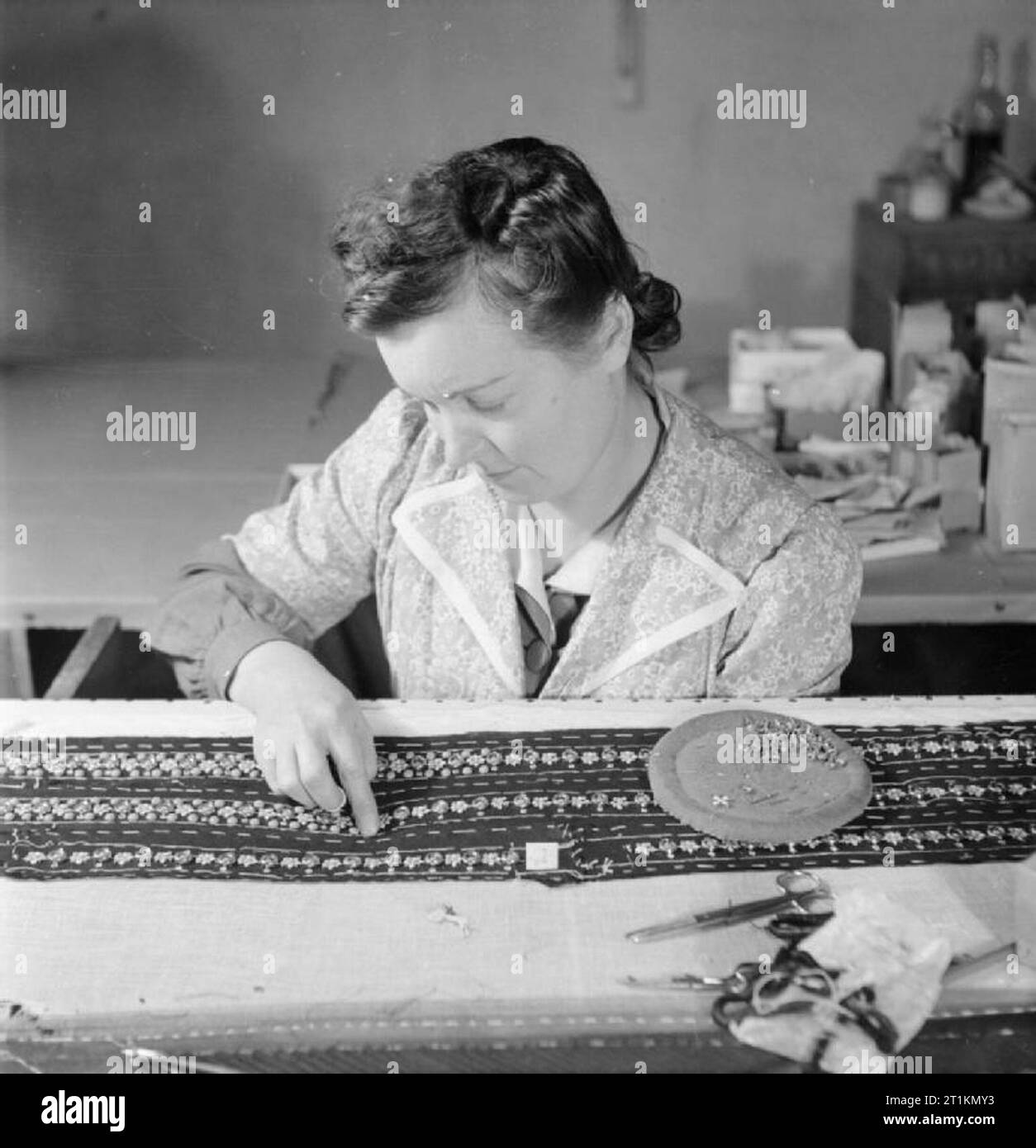 London Fashion Designers- the work of Members of the Incorporated Society of London Fashion Designers in Wartime, London, England, UK, 1944 In the workrooms of the fashion designer Norman Hartnell in London, a skilled worker applies by hand blue and gold studs in strips to fabric which is to be used for a black velvet evening gown. Stock Photo