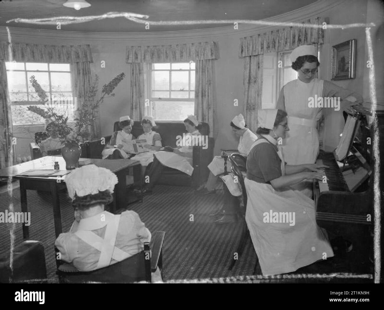 Mansion Becomes Maternity Home- Life at Brocket Hall, Welwyn, Hertfordshire, 1942 Nurses read or play the piano as they relax in their sitting room at the end of a busy day at Brocket Hall maternity hospital. Stock Photo