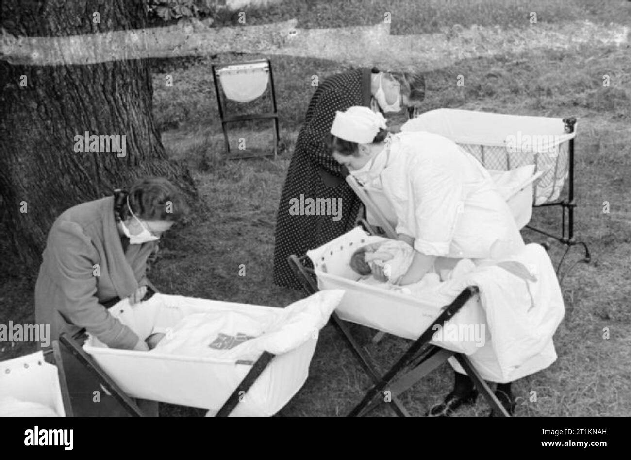 Mansion Becomes Maternity Home- Life at Brocket Hall, Welwyn, Hertfordshire, 1942 New mothers and a nurse collect their babies for 'feeding time'. The babies have been enjoying an open air snooze. The women are all wearing surgical masks to prevent the spread of germs. Stock Photo