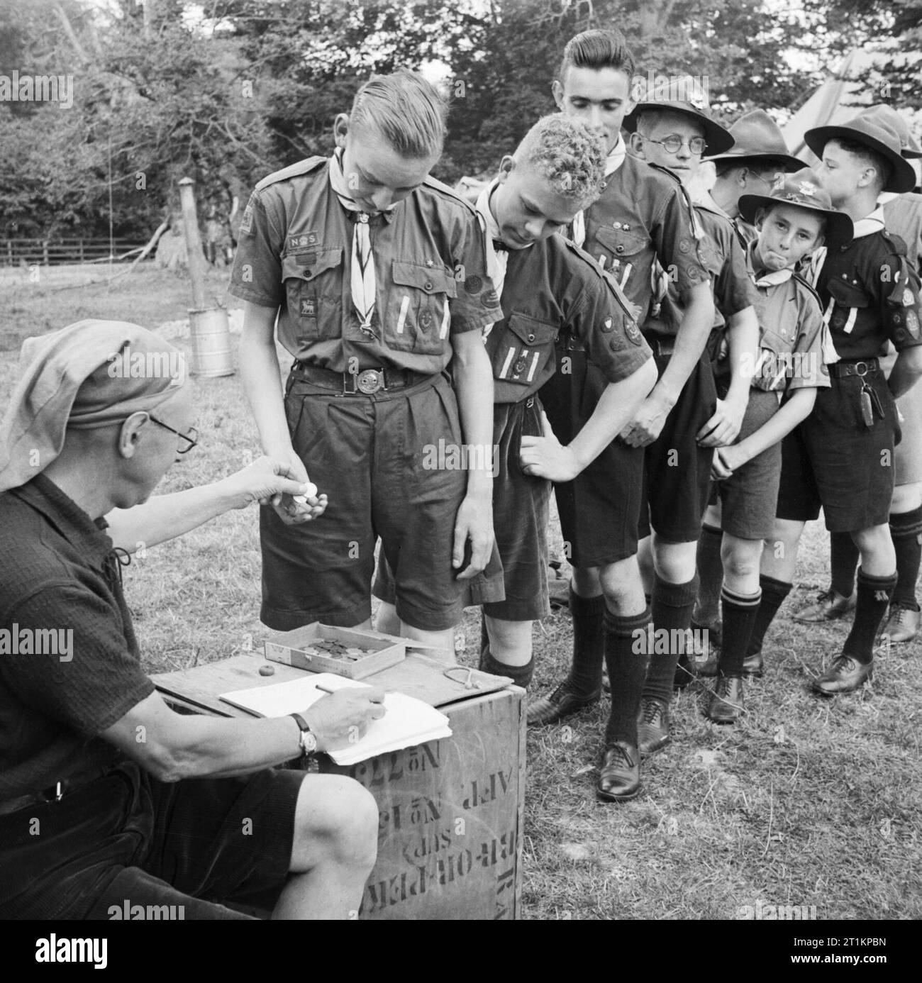 Pay Day for Boy Scouts at a fruit-picking camp near Cambridge in 1943. Saturday is Pay Day at the fruit-picking camp. Boy Scouts queue up in a pay parade to collect their pocket money from the Scout master. Over 14s get half a crown, whilst under 14s receive a shilling. Stock Photo