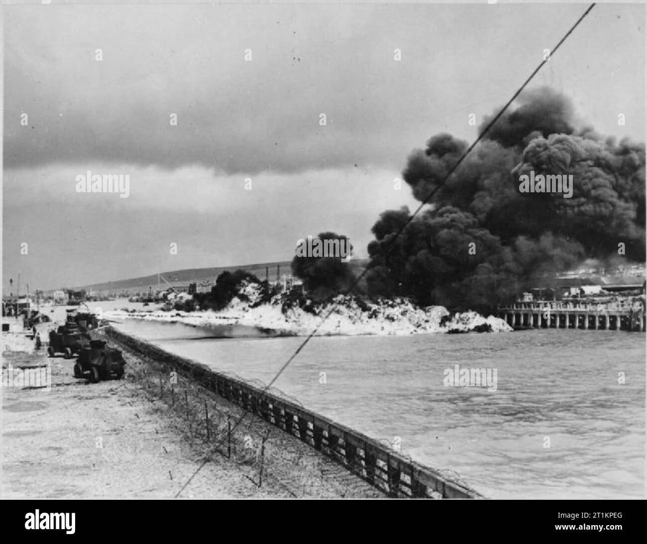 Petroleum Weapons Against Invasion- a Demonstration of Anti-invasion Defences, UK, 1945 A demonstration of 'Fougasse', somewhere in Britain. A group of flame-throwing tanks can be seen lined up on the left hand side of the photograph. They are firing across a river or waterway. A large cloud of smoke can be seen, rising up from the columns of fire. The original caption states that this weapon 'released one ton of burning oil when fired. Developed by the Petroleum Warfare Department in the summer of 1940, it was installed within three weeks of the conception of the idea'. Stock Photo