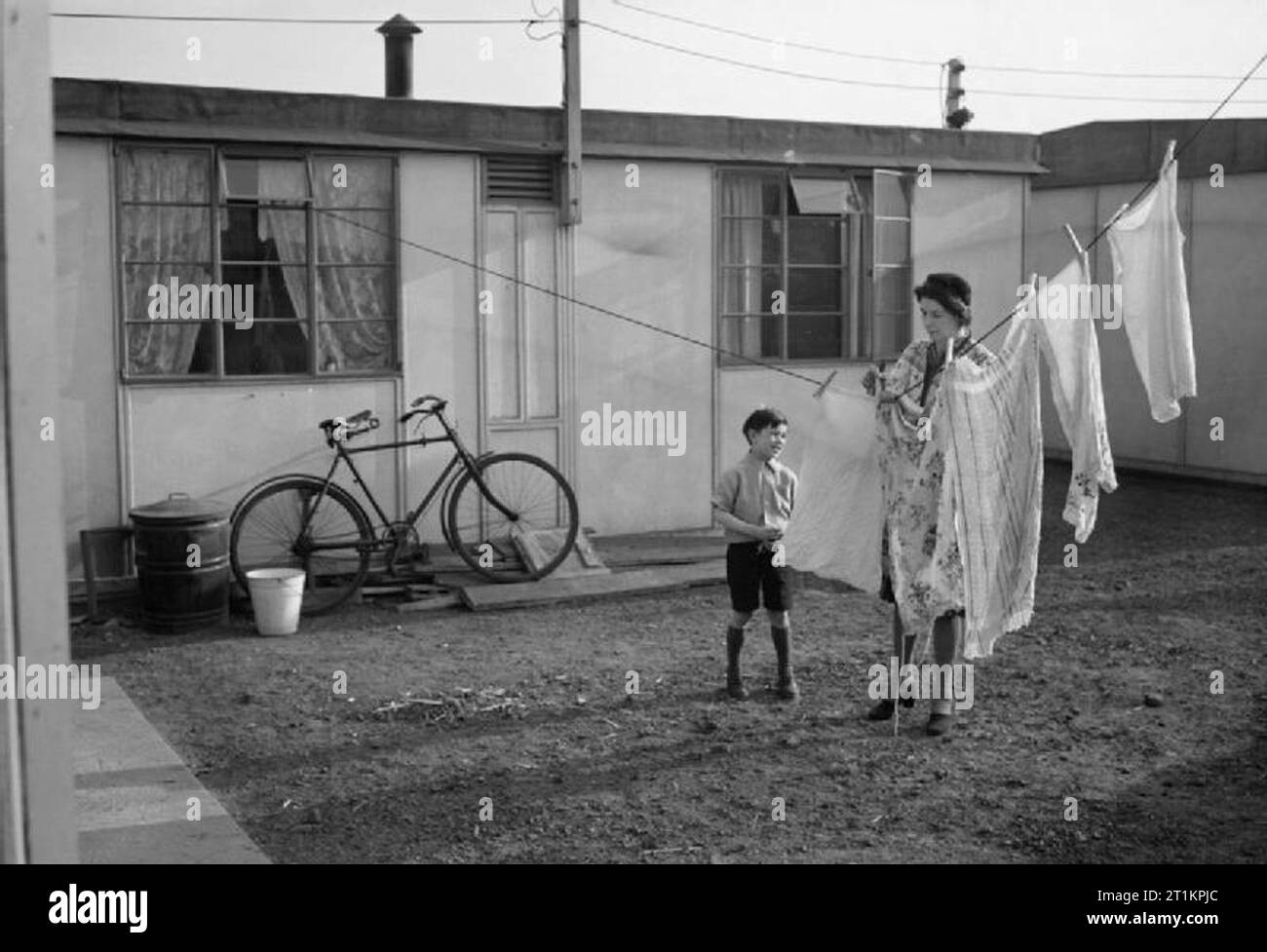 Post War Planning and Reconstruction in Britain- the Construction of Temporary Housing A mother hangs out the family washing outside a newly completed Uniseco prefabricated emergency house. Stock Photo