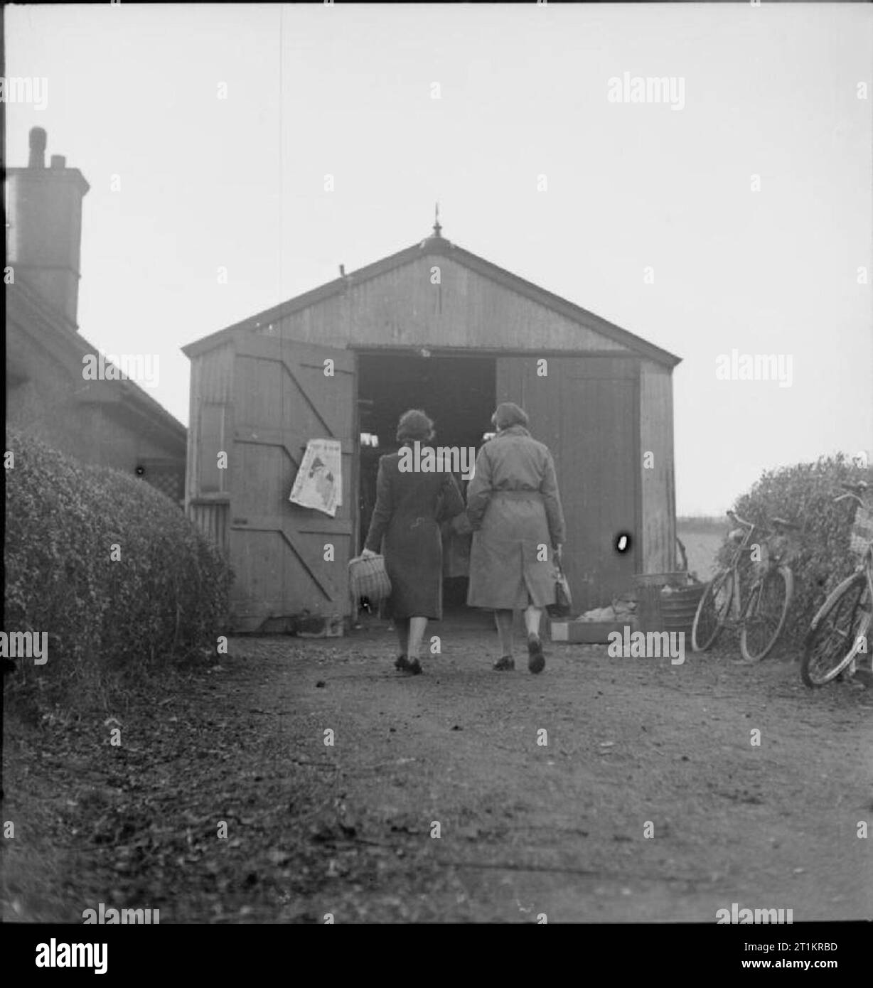 Sten Gun Production in Britain, 1943 Two part-time war workers enter their 'factory at the beginning of their shift. The building is an old hen house which is being reused as a venue for the manufacture of breech blocks from solid steel bars. This 'factory' was owned by Mr C W (Charles) Packard, an engineer and former haulage contractor, and was probably in Welwyn Garden City. Stock Photo
