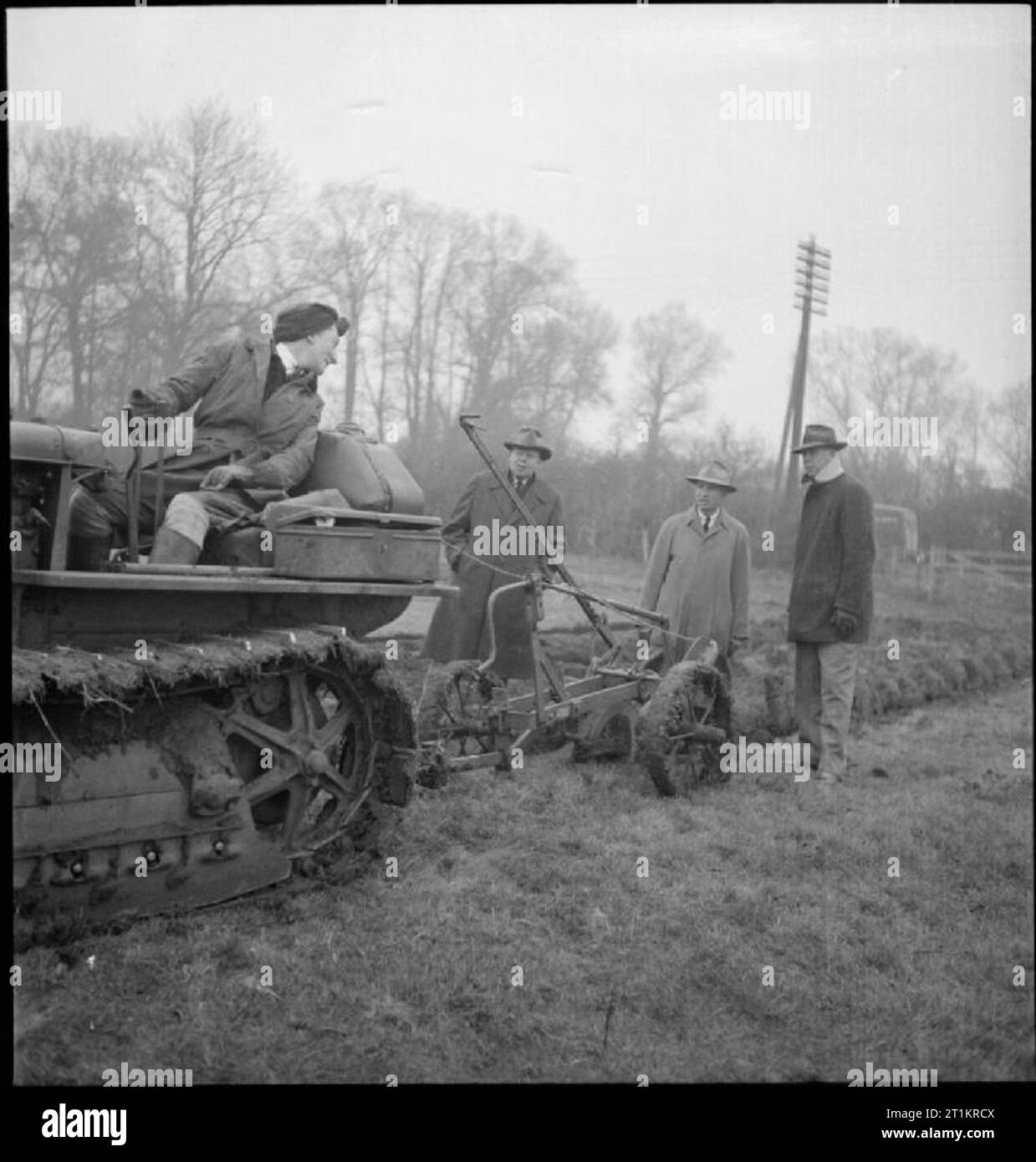 American Farmers Visit Britain- Lend-lease Equipment in Action, UK, 1943 Land Girl Kathleen Johnson demonstrates the ploughing capabilities of a Caterpillar D2 tractor and Oliver deep digger plough to Mr Heline, Mr Howard and Mr Robinson on grassland, somewhere in Buckinghamshire. The plough is from the Oliver Farm Equipment Company of Chicago. Stock Photo