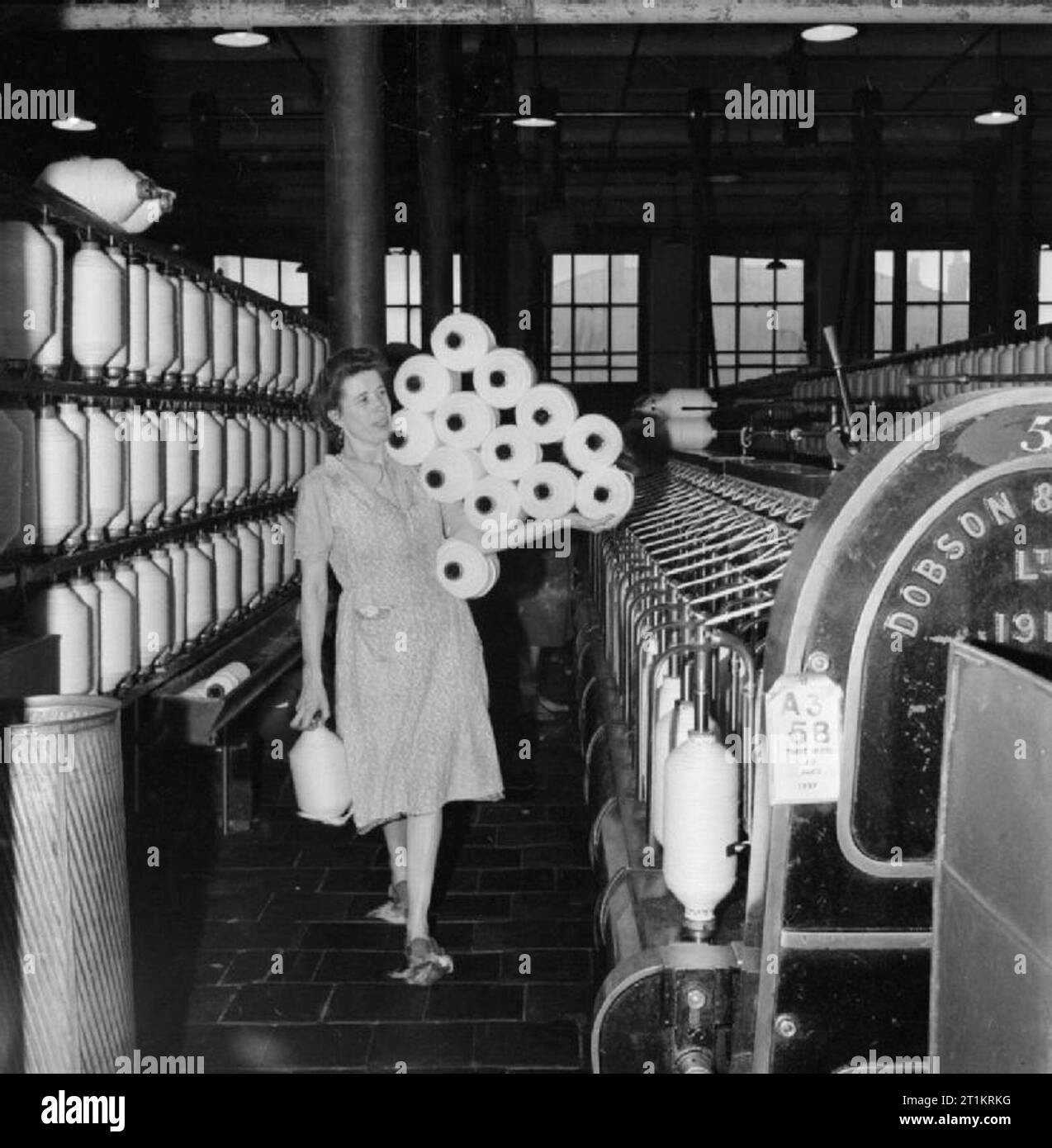 The British Cotton Industry- Everyday Life at a British Cotton Mill, Lancashire, England, UK, 1945 Cotton worker Mrs Bannister carries 14 large bobbins (13 in one arm and 1 in the other hand!) from the 'intermediate to the roving frames' at a cotton mill, somewhere in Lancashire. Stock Photo