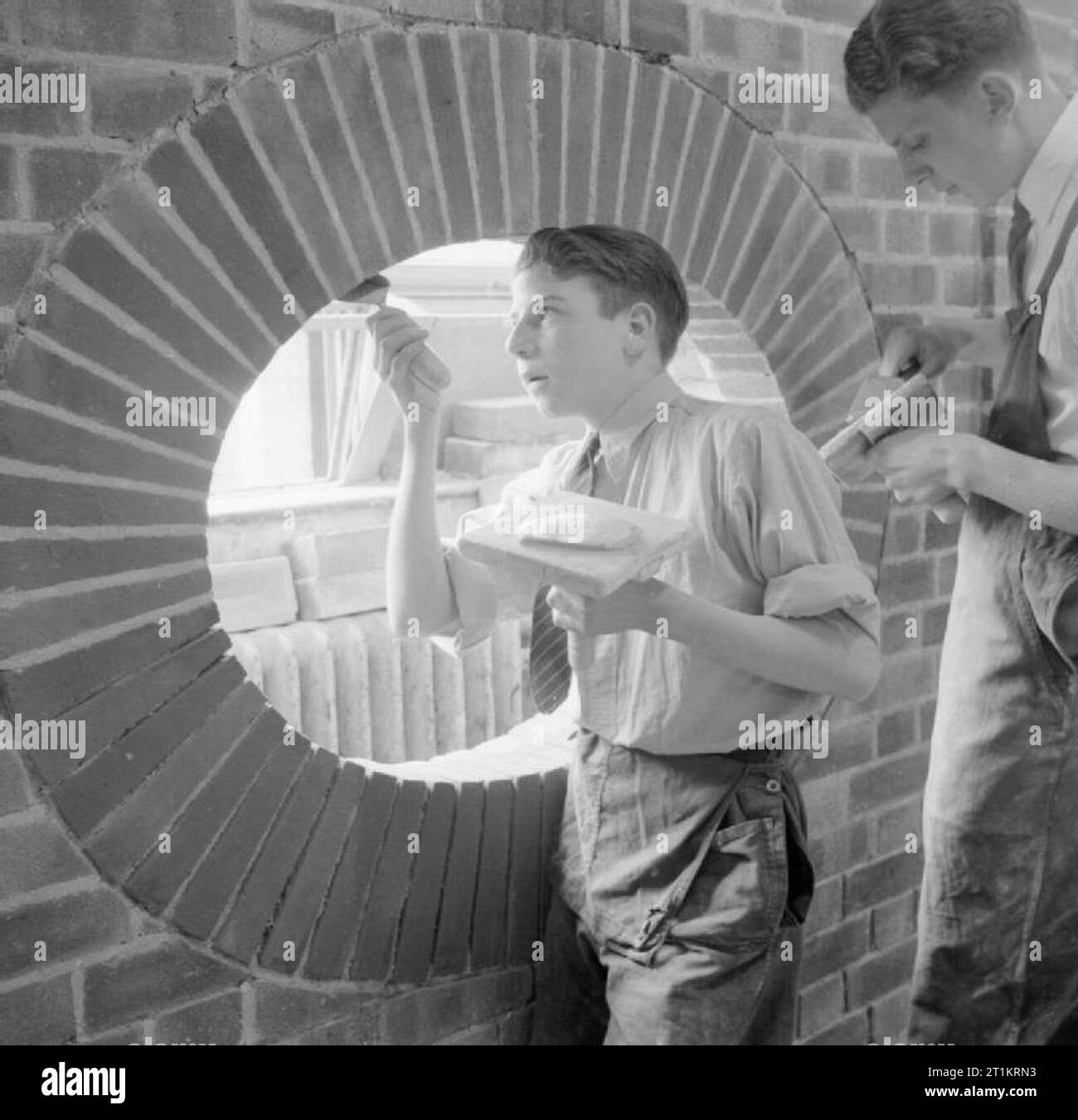 Technical School- Training at Tottenham Polytechnic, Middlesex, England, UK, 1944 Boys learn bricklaying at Tottenham Polytechnic. Here, one pupil is pointing bricks which have been set vertically in a circular shape, described in the original caption as 'an elliptical arch', creating a 'pothole' in a wall. Stock Photo