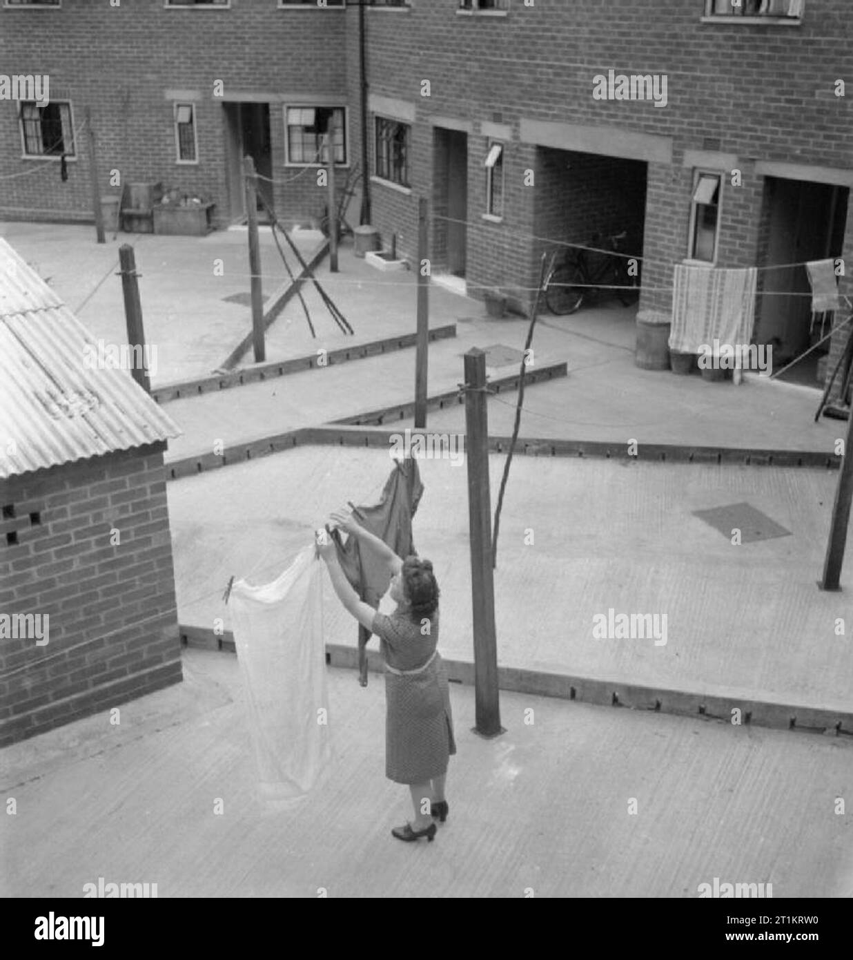 The Cottages of Freefolk- Life in the Village of Freefolk, Hampshire, England, UK, 1943 A woman hangs out her washing in the back yard of her cottage in Freefolk, Hampshire. Each cottage has a vegetable and flower garden at the front of the house, but a concrete yard has been provided at the rear of the houses, complete with permanent clothes line posts. Stock Photo