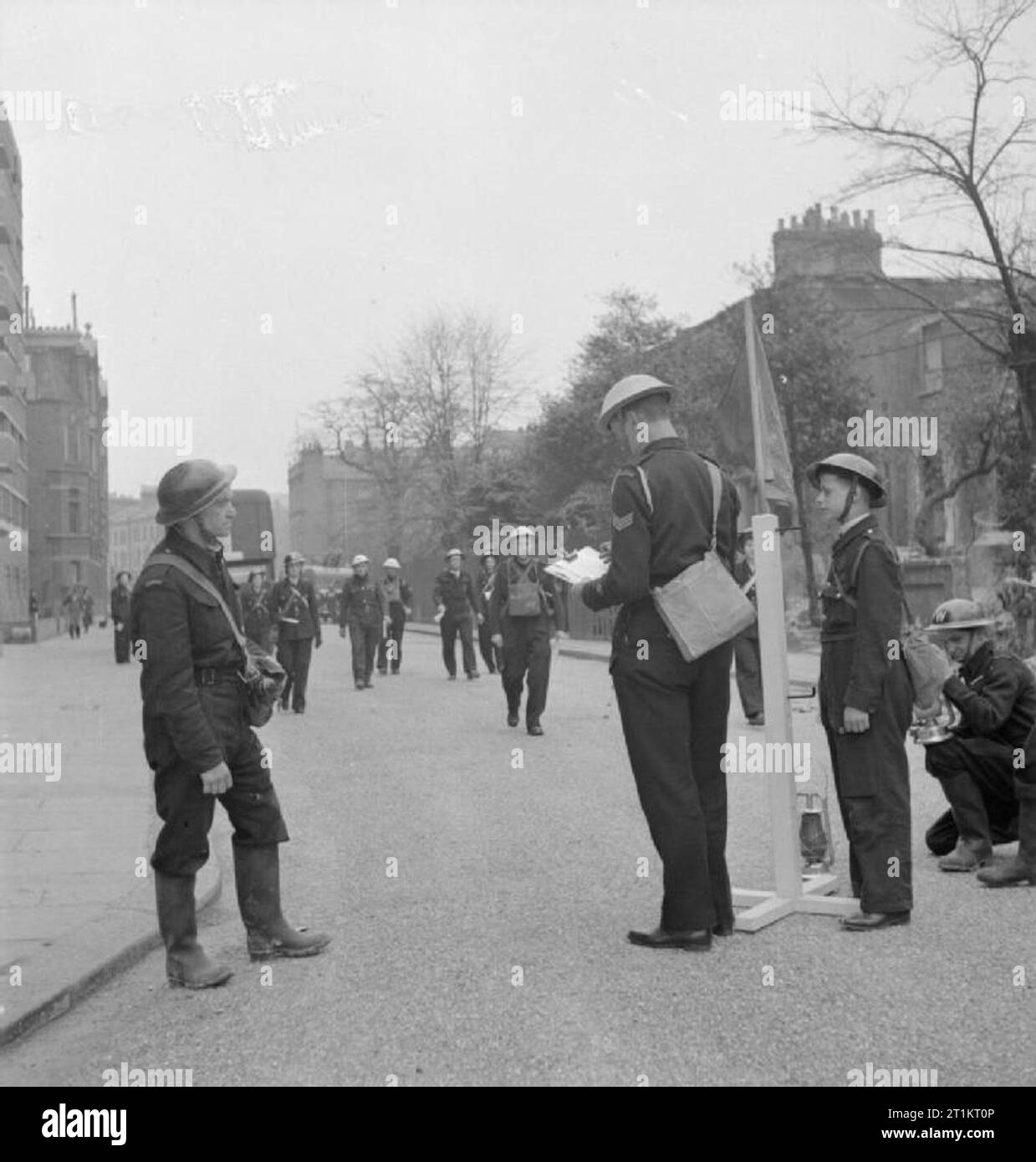 The Reconstruction of 'an Incident'- Civil Defence Training in Fulham, London, 1942 Leaders of the various services arrive and report to the incident officer. On the left can be seen the ARP Warden who originally reported the incident. The incident officer wears a blue helmet, has a blue lamp and a blue flag, to himself and the incident control point clearly visible to all Civil Defence workers involved. A boy messenger can also be seen. This photograph was taken on North End Road, at the junction with Conan Street (now West Cromwell Road), looking South towards Fulham. Just visible on the lef Stock Photo
