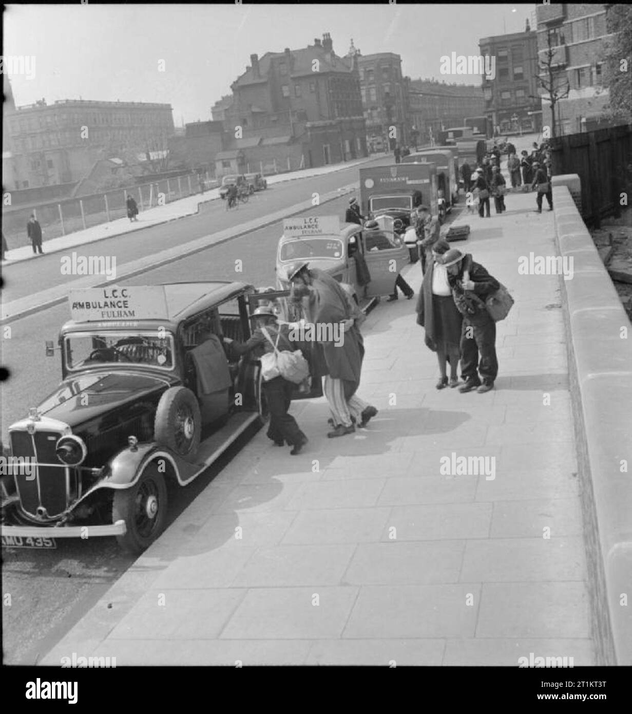 The Reconstruction of 'an Incident'- Civil Defence Training in Fulham, London, 1942 Walking wounded cases are led to waiting ambulance cars by members of the 'light rescue' teams, as behind them, stretcher cases are carried to ambulances. This photograph was taken on West Cromwell Road/Conan Street, looking West towards North End Road, which crosses Conan Street at right angles. Conan Street becomes Talgarth Road at this junction. West Kensington Court is visible on the right. Stock Photo