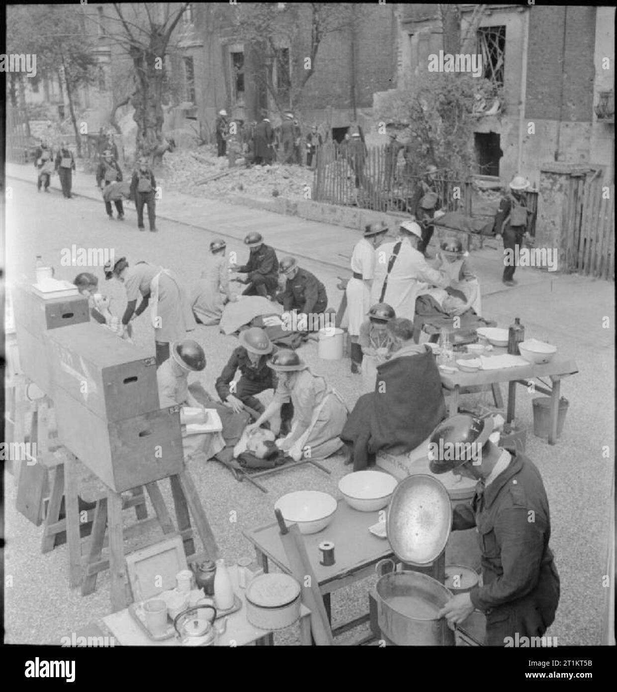 The Reconstruction of 'an Incident'- Civil Defence Training in Fulham, London, 1942 A mobile medical unit has been set up at one end of the street in order to grade and treat casualties as they are brought from the incident. Behind them, more rescue work is being carried out by Civil Defence workers and two stretcher bearers can just be seen bringing another casualty to the medical unit. This photograph was taken on Edith Villas, looking from the West Cromwell Road end, towards Edith Road. West Kensington Court (not visible) is on the left. Stock Photo