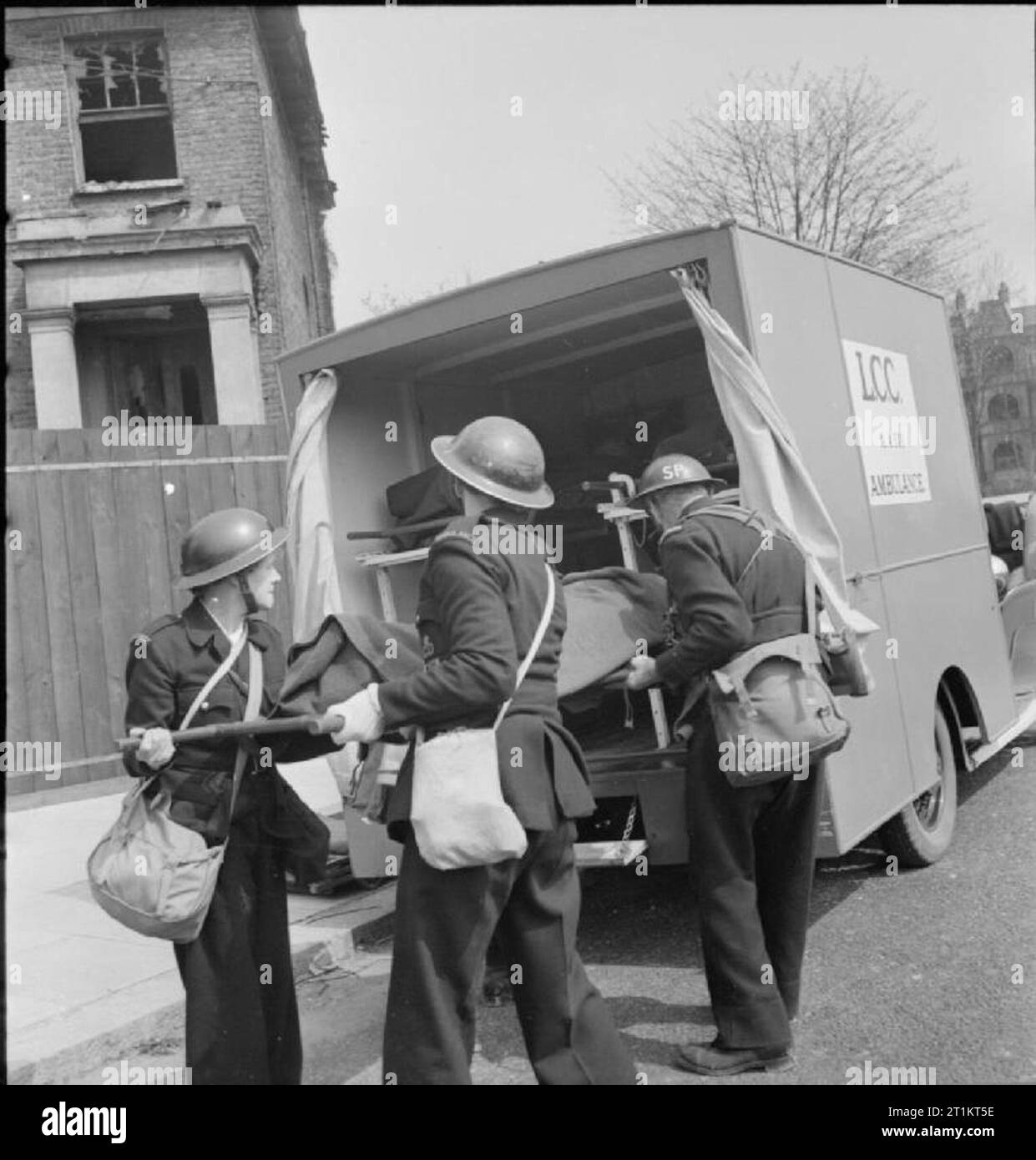 The Reconstruction of 'an Incident'- Civil Defence Training in Fulham, London, 1942 Two female ambulance drivers help men of the 'light rescue' stretcher party to slide a stretcher case into a waiting ambulance. These casualties will then be taken either to the first aid post in a nearby school, or transported to hospital. A window-less bomb-damaged house is just visible behind them. This photograph was taken on West Cromwell Road/Conan Street, where it joins Edith Villas. Stock Photo