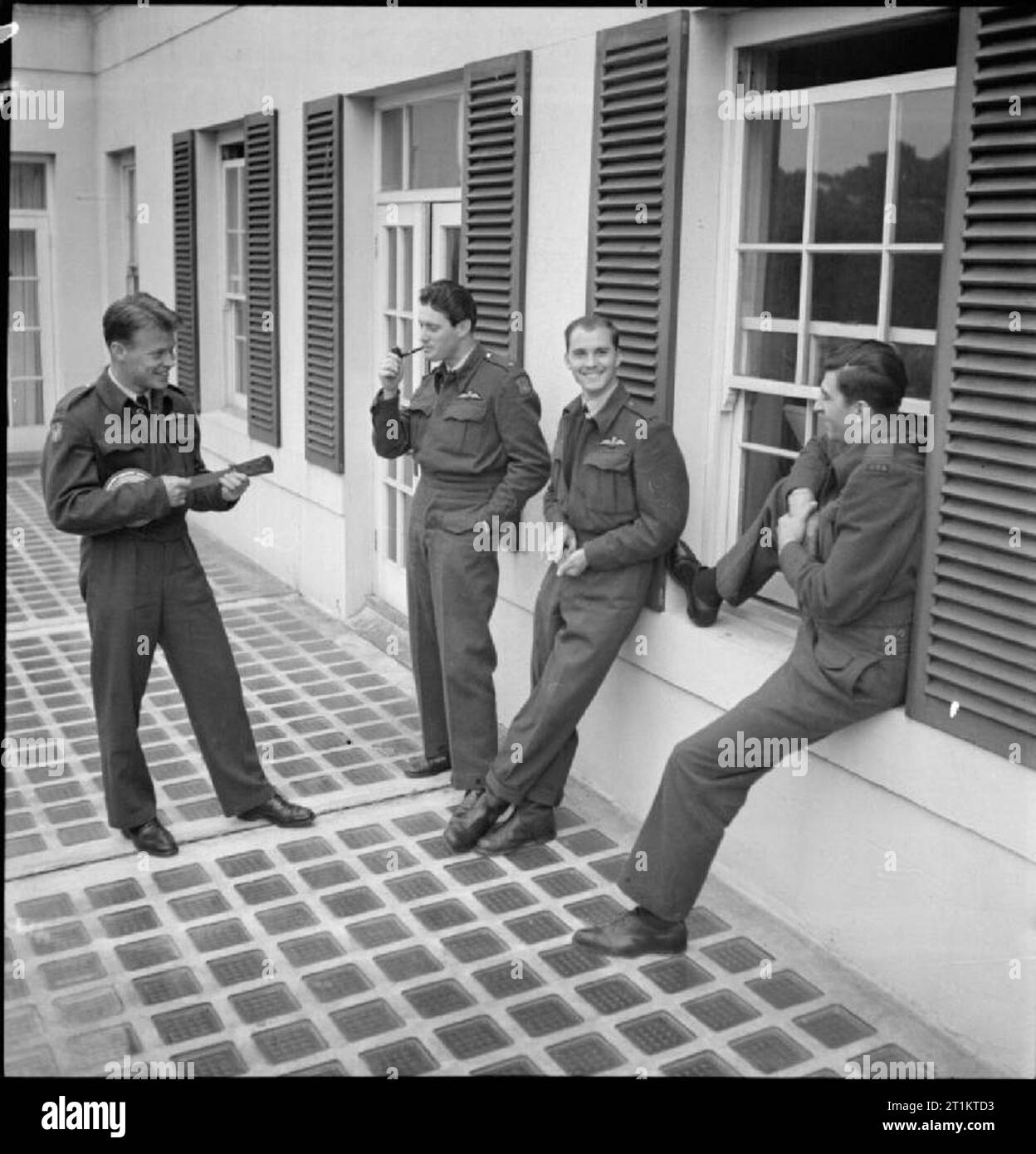 Americans in Britain- the work of No 121 (eagle) Squadron RAF, Rochford, Essex, August 1942 Flying Officer Osbourne plays a tune on his banjulele as entertainment for his Eagle Squadron colleagues on the terrace of the old English house in which they are billeted. Left to right, the 'audience' is: Pilot Officer Kearney (smoking a pipe), Pilot Officer Slater and Pilot Officer Padget (seated on the window sill). Stock Photo