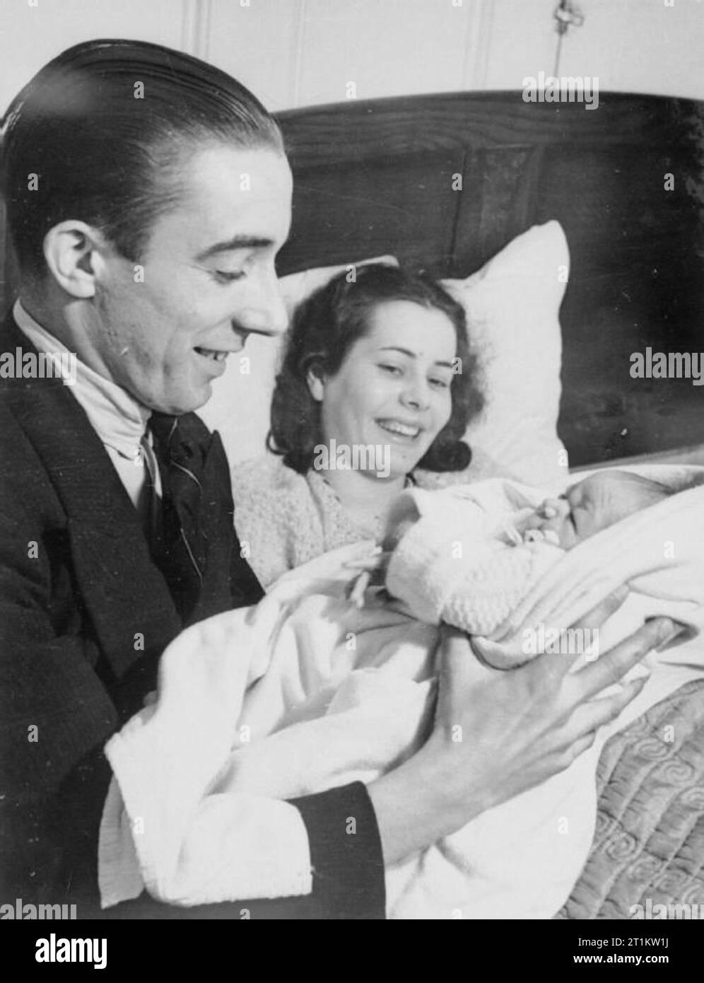 An Expectant Mother in Wartime, London, England, March 1940 Mr Bentley holds his newborn son, as his wife Vera rests in bed behind him at their home in Goldhawk Road, West London, March 1940. Stock Photo