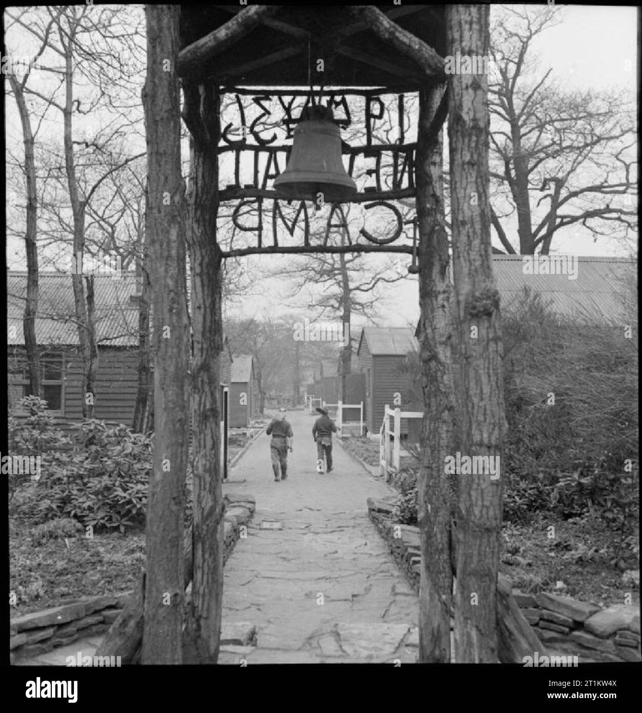 Wakefield Training Prison and Camp- Everyday Life in a British Prison, Wakefield, Yorkshire, England, 1944 The entrance to New Hall Camp at Wakefield Training Prison. Two inmates walk down the path towards their huts, carrying garden tools. According to the original caption, the land for this camp was acquired in 1933. 'Parties of prisoners conveyed daily from Wakefield Prison cleared the woodland for cultivation and gradually erected the camp'. Stock Photo