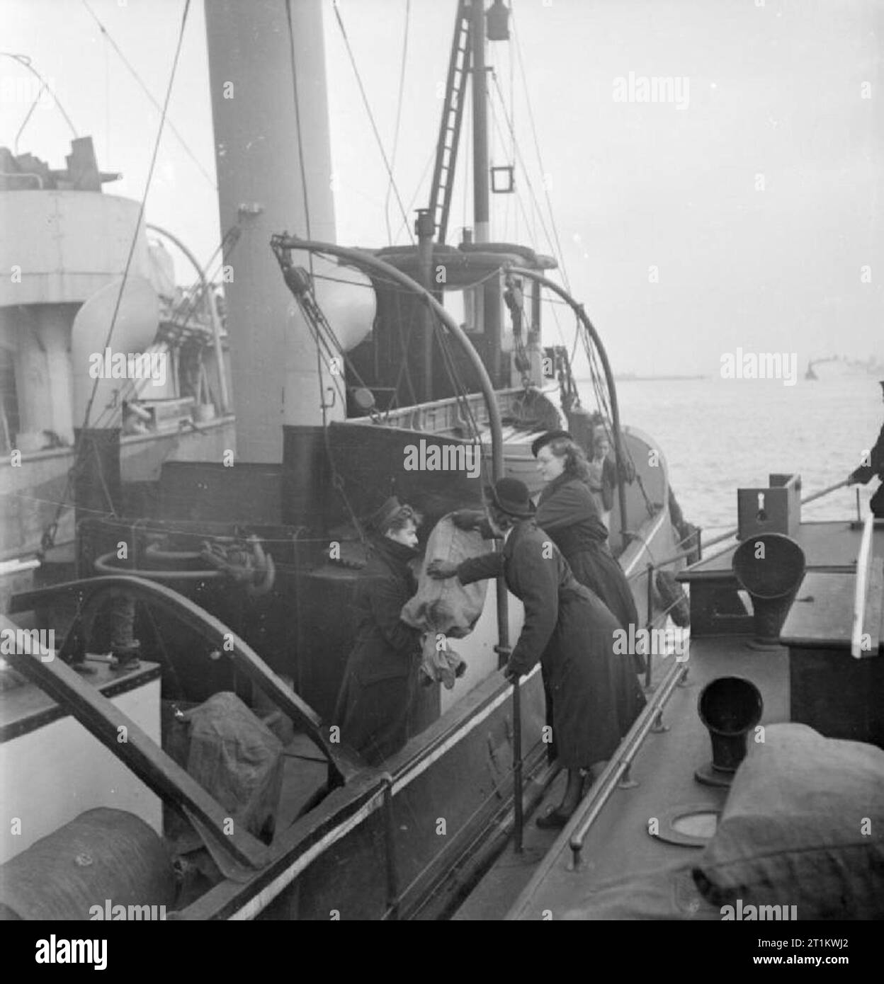 Women's Royal Naval Service- Wrens With the Fleet Mail, England, UK, November 1944 Two Wrens of the Fleet Mail deliver mail to a vessel moored in the harbour on a cold November day. They are passing a sack across to the vessel from the deck of the Mail Boat. Stock Photo