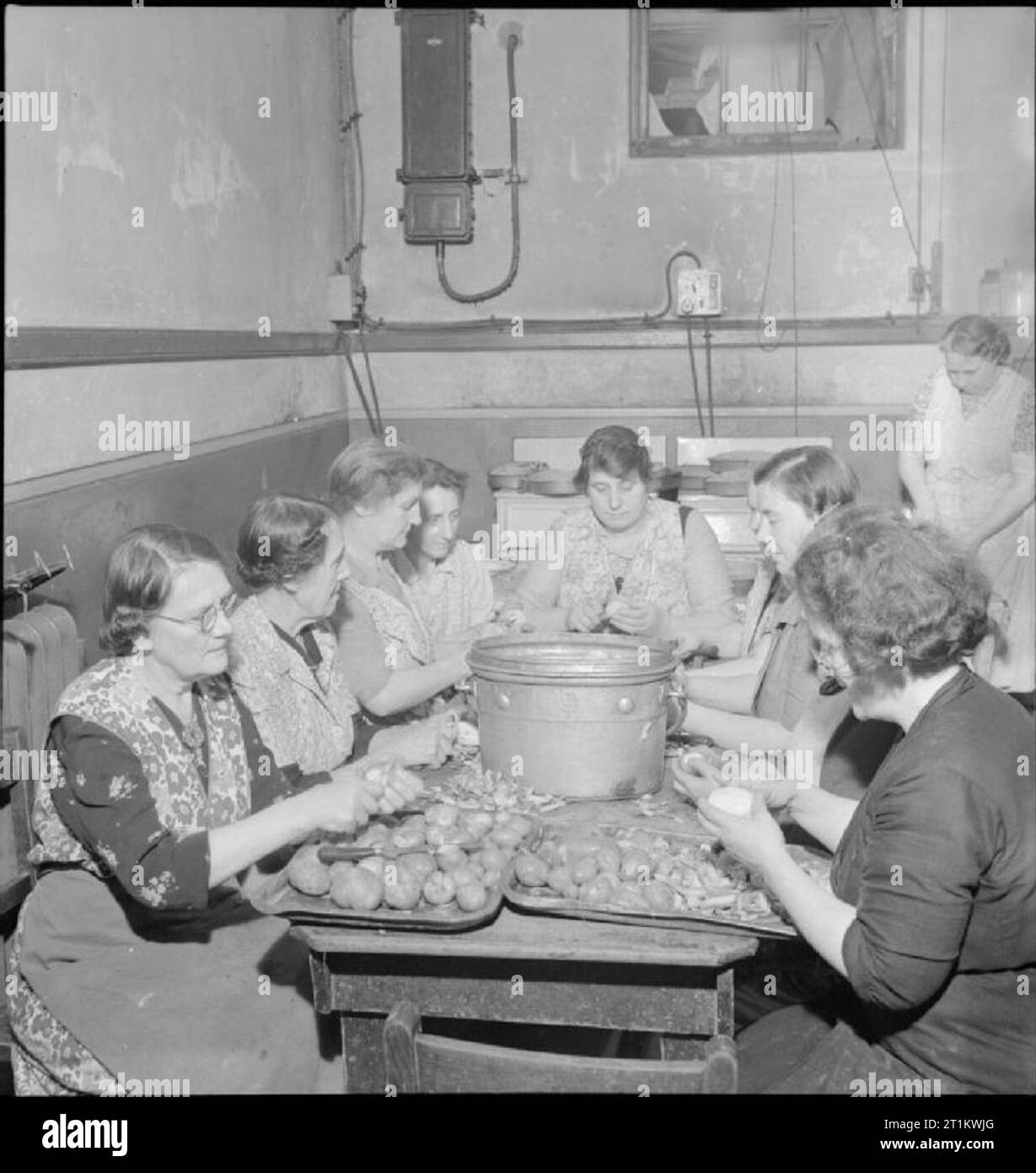 Woolmore Street Restaurant- Eating Out in Wartime London, 1942 Women at work preparing vegetables in the kitchen of the British Restaurant at Woolmore Street. Left to right they are: Mrs F Malyon (aged 59), Mrs C Pude (aged 64, a cigar worker in peacetime), Mrs Florence Skinner, Mrs Davison (once demonstrated cleaning materials), Mrs J Harrop (ran a corn chandler and grocer's store), Doris Prigge (previously in the catering trade), Miss Barkwith, Miss Violet Hancock and Mrs Turley. Another woman can be seen in the background. Stock Photo