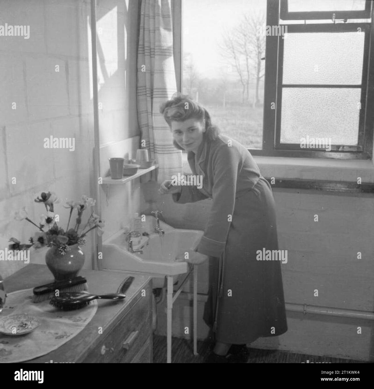Workers Welfare at a Royal Ordnance Factory- Life at Rof Bridgend, January 1942 A female war worker cleans her teeth in the bedroom she shares with another woman in the war workers hostel at ROF Bridgend. According to the original caption, hot and cold water and central heating were laid on in all the rooms. Stock Photo