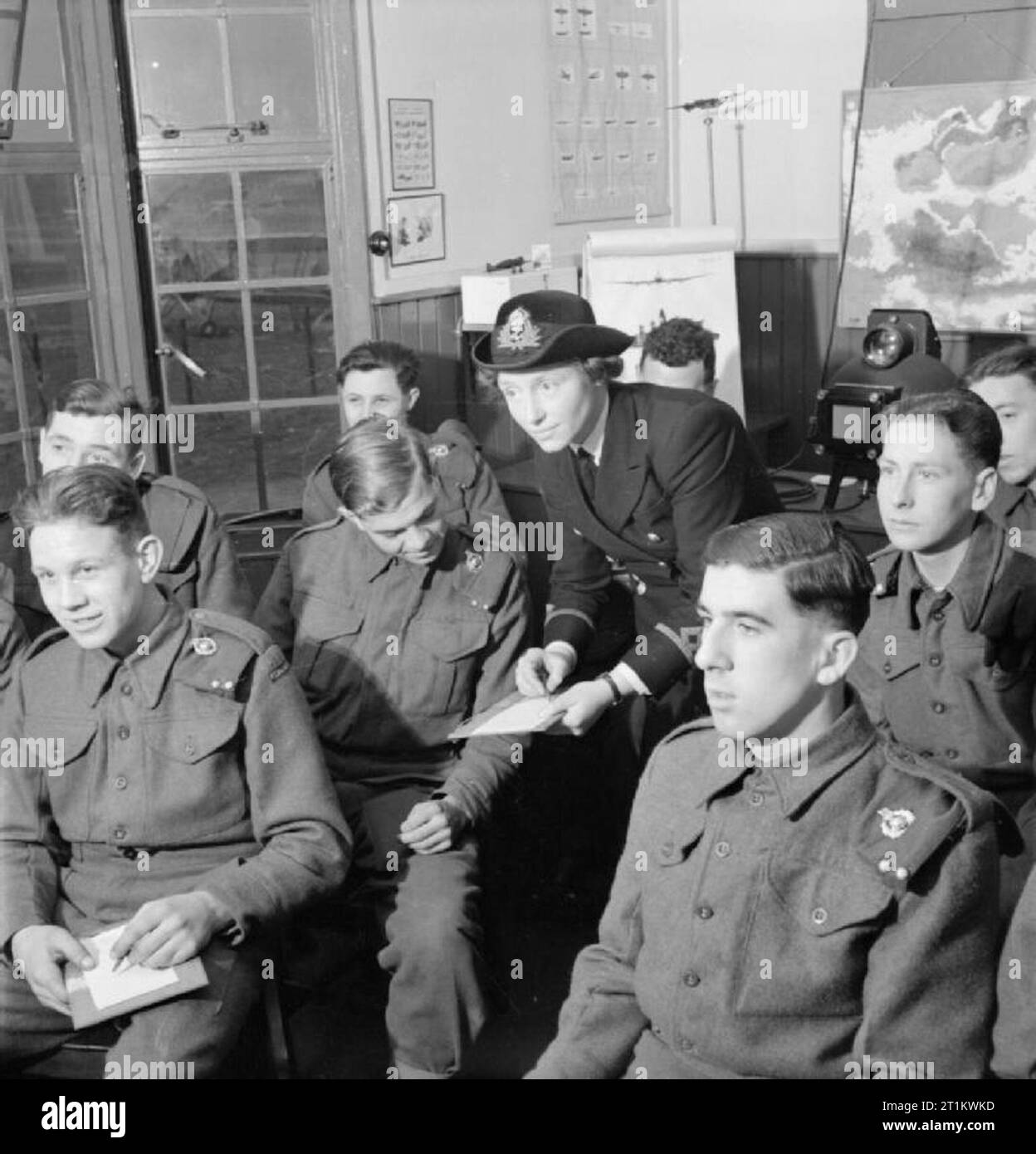 Women's Royal Naval Service- With the Fleet Air Arm, Scotland, 1943 Third Officer Ingledew, WRNS, encourages gunners of the Station Defence to draw various aircraft types from memory as part of her daily hour-long lecture on aircraft recognition. The epidiascope used to project pictures of aircraft onto the screen as part of this class can be seen in the background. Drawings are judged on the recognition of outstanding features of all aircraft types, not on artistic merit! According to the original caption, a similar course is being considered for Fleet Air Arm personnel on the recognition of Stock Photo