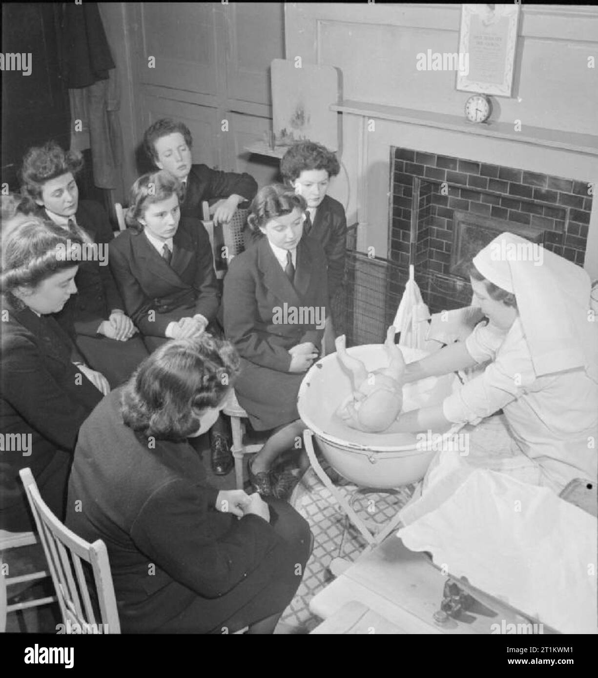 Wrens Learn Mothercraft- Members of the Women's Royal Naval Service Receive Training From the Mothercraft Training Society, London, England, UK, 1945 A group of women of the WRNS receive a lesson in bathing a baby from Matron Miss Maslen-Jones of the Mothercraft Training Society, probably at the MTS headquarters in Highgate, London. The original caption describes the correct way to bath a baby as follows: 'The baby is uncovered and soaped thoroughly going well into the creases, and then lifted straight into the bath. Soap is never used on baby's face and the head is always washed over the bath Stock Photo