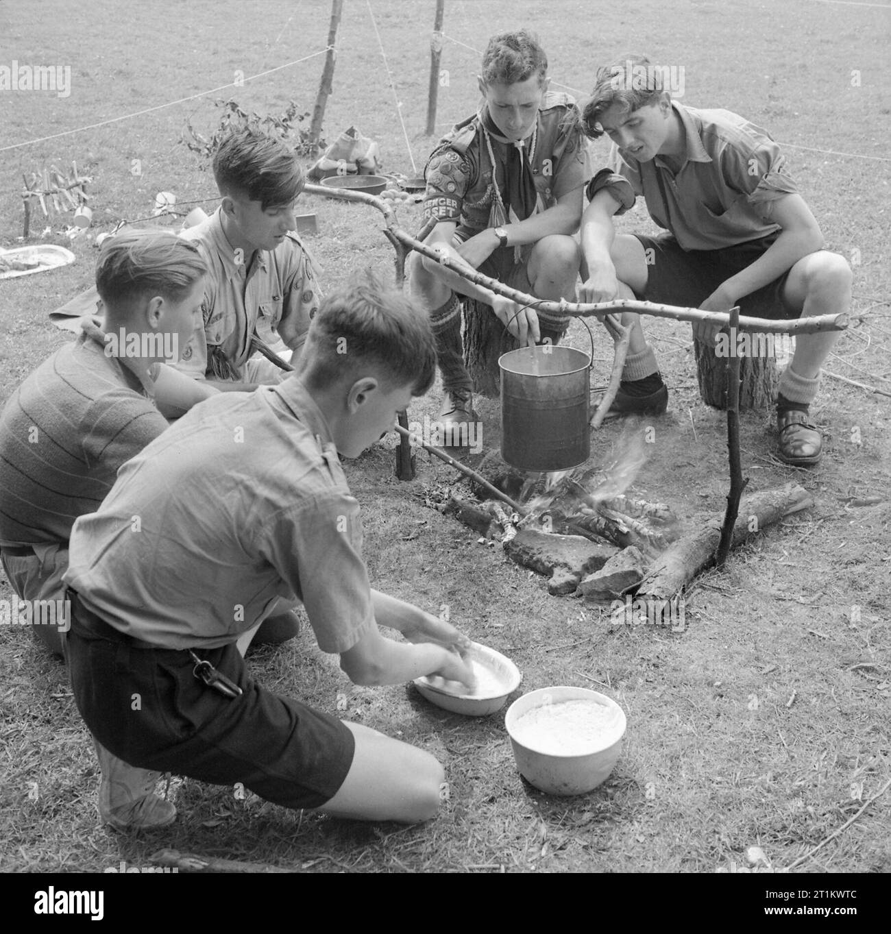 Youth Gathering- Residential Training For Youth Organisations, Sidcot School, Winscombe, Somerset, England, UK, 1943 Five Boy Scouts make bread over a camp fire as part of a week-long youth training course being held at Sidcot School in Somerset. In the foreground, one Scout is making the dough, whilst behind him another stirs the steaming billy can hanging over the camp fire. Stock Photo