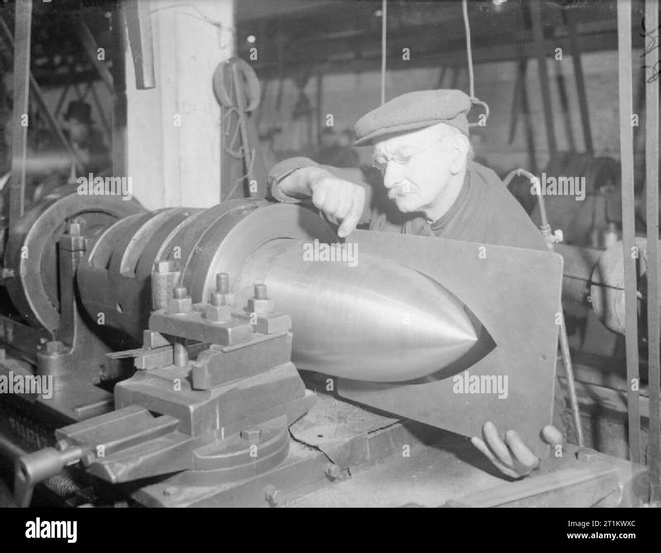 At work in a British Shell Factory, England, C 1940 Bertie Beale, aged 64, works on a large shell at a factory somewhere in England. Mr Beale has been working in shell production since 1899 and between 1896 and 1900 was an artillery man in the City of London Volunteers. Stock Photo