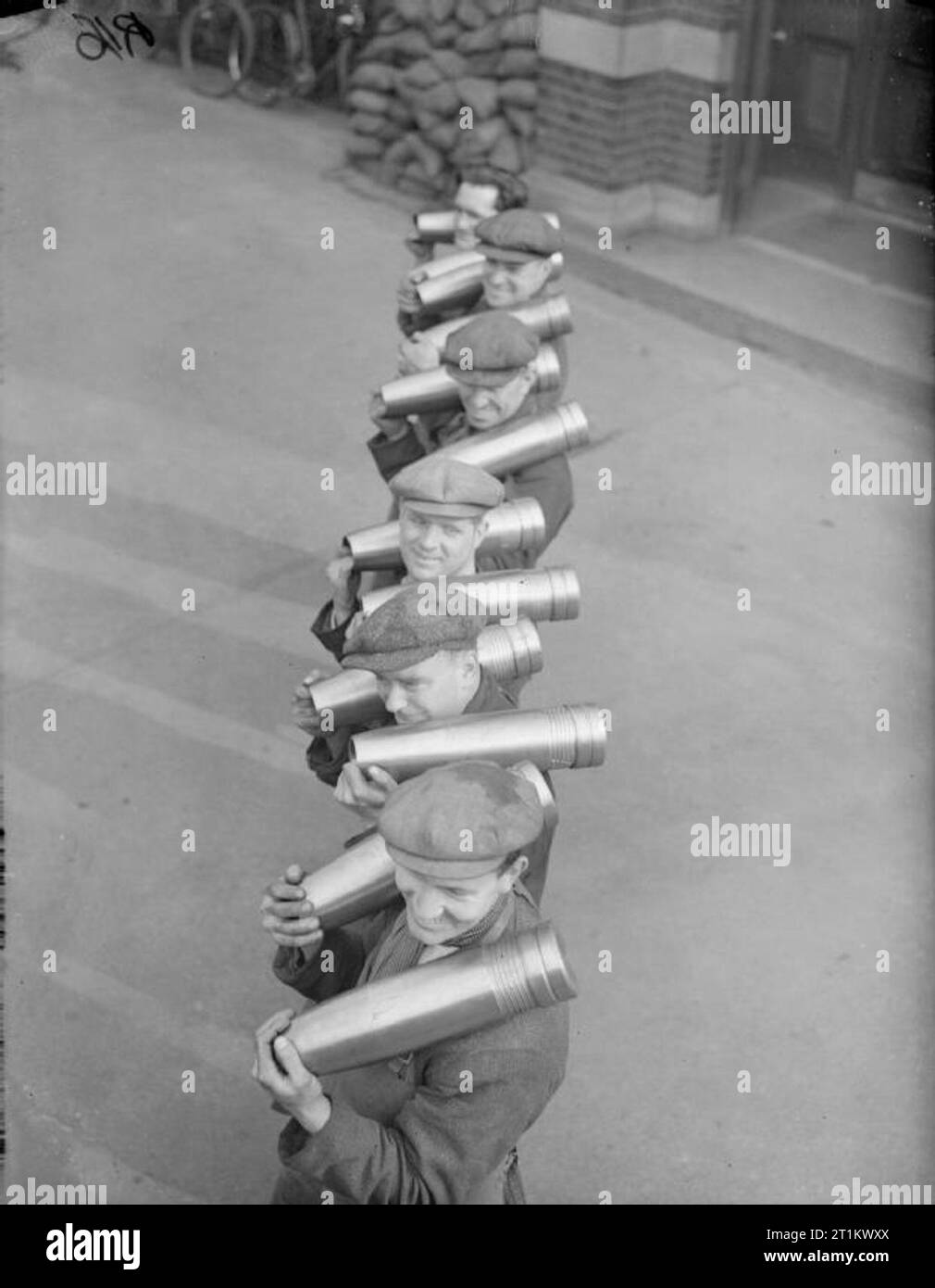 At work in a British Shell Factory, England, C 1940 A row of happy munitions workers balance medium sized shells on their shoulders, outside a British shell factory. Stock Photo